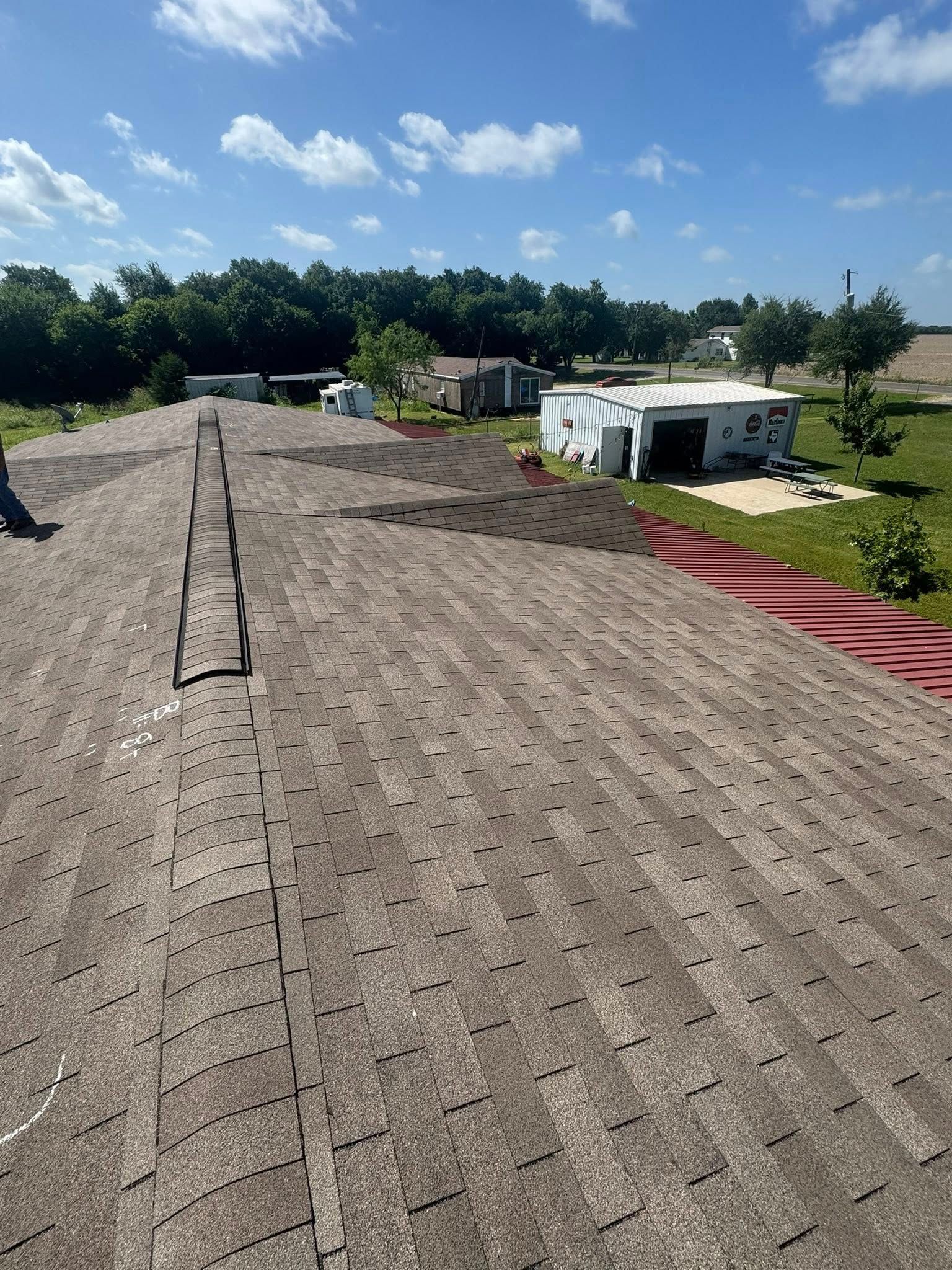 Rooftop under repair with brown shingles, a ladder, and white RVs in a sunny rural setting