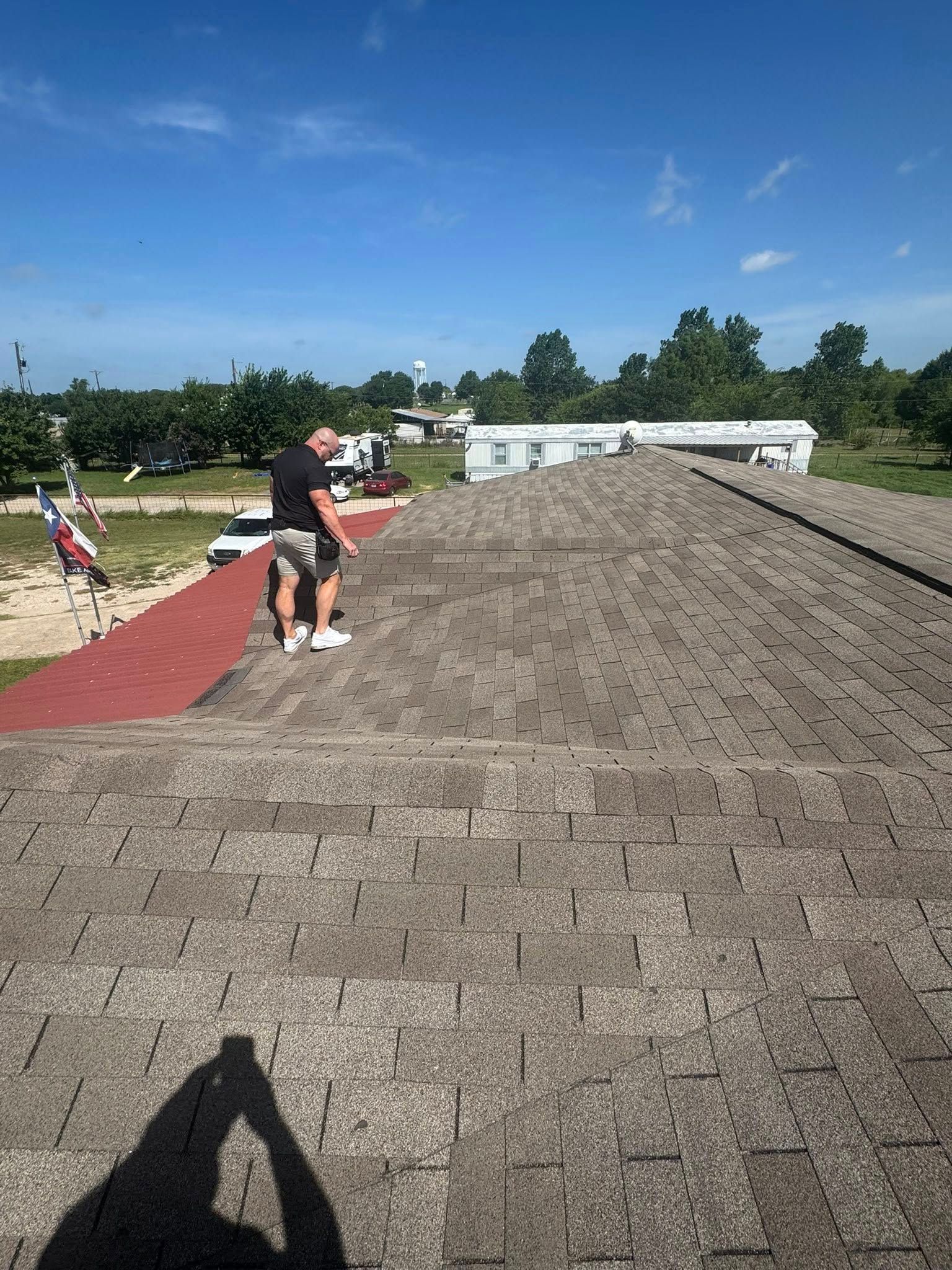 Workers installing roofing felt on a steep shingled roof under a bright blue sky