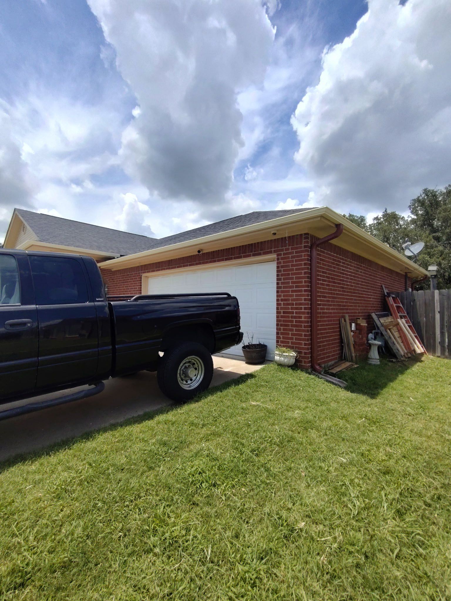 Black pickup truck parked beside a brick garage under a cloudy sky, with lawn in the foreground