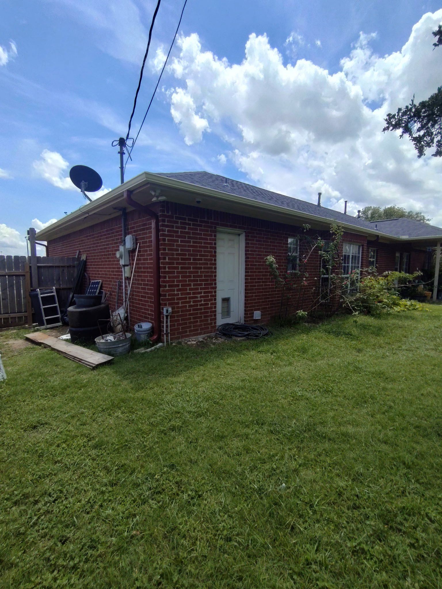 Brick house with green roof, white door, and satellite dish in a grassy yard under a cloudy sky