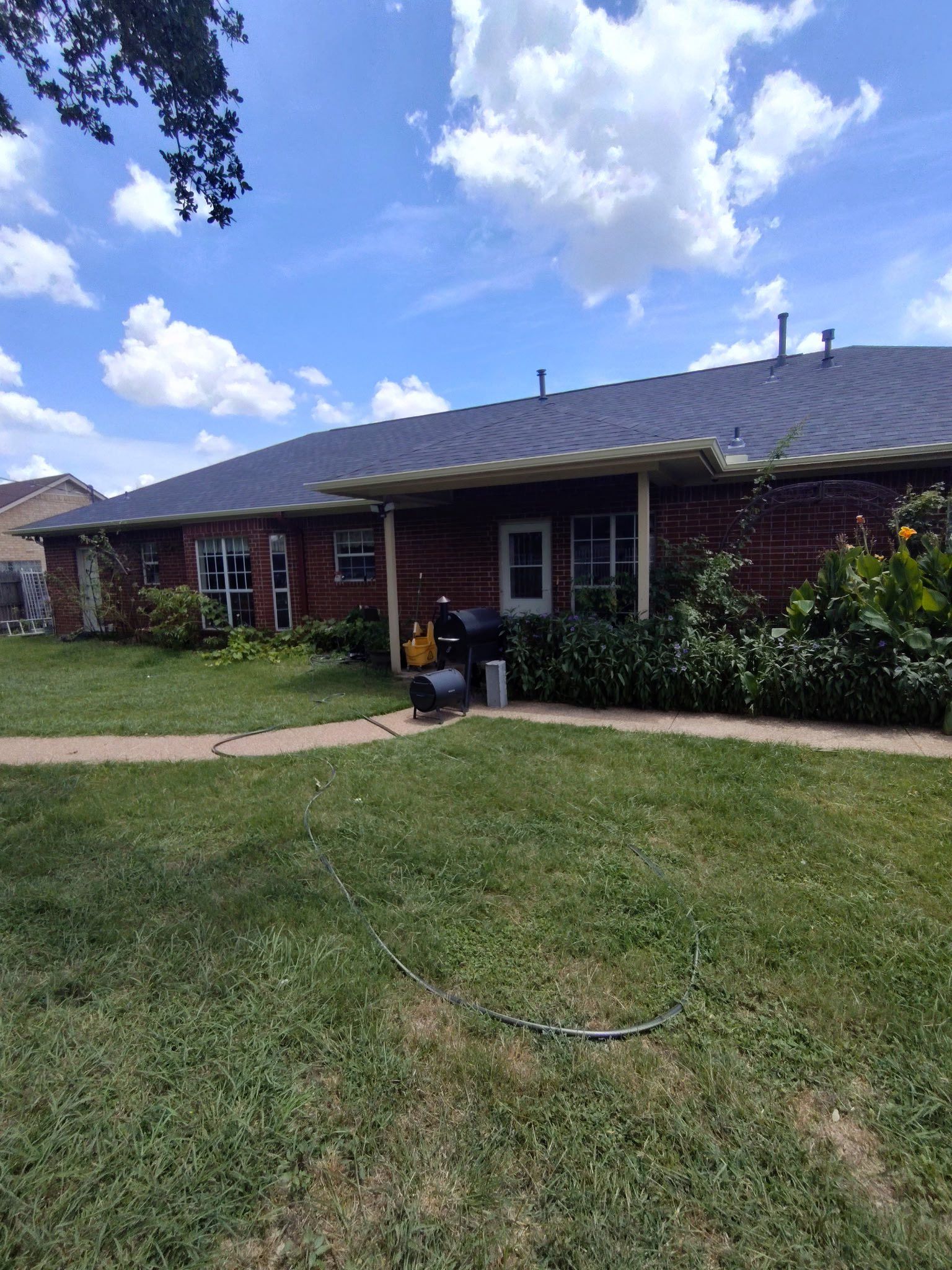 Single-story brick house with a lawn, front porch, and bright blue sky with clouds
