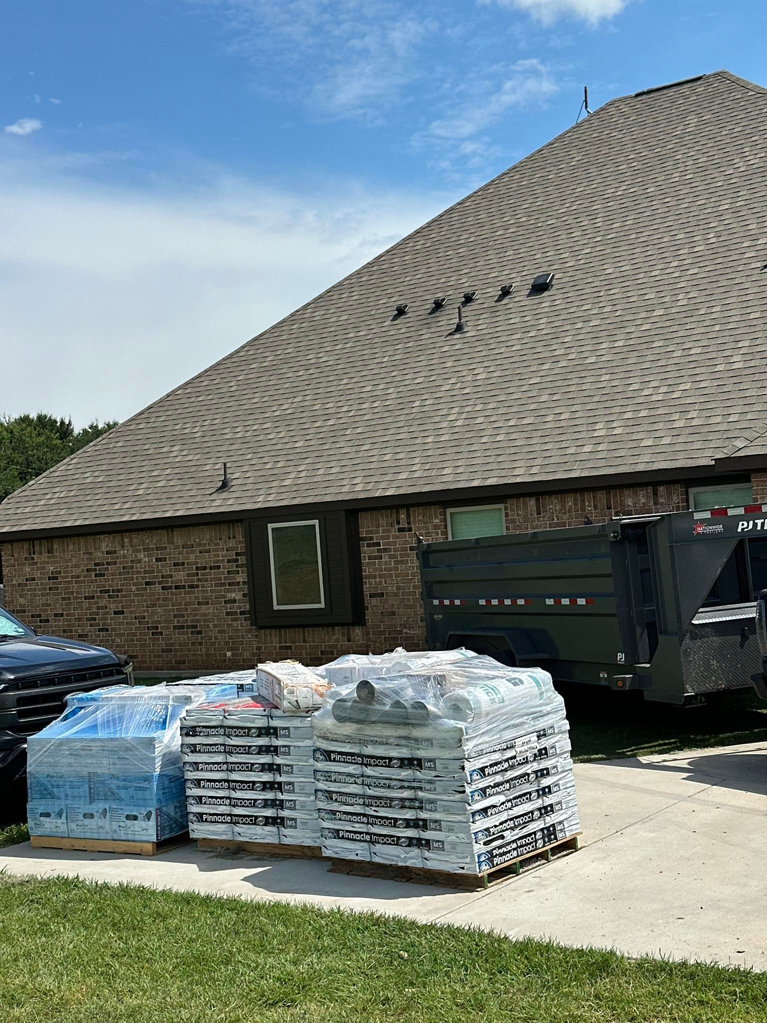 Stacked pallets of bottled water beside a brick building and dumpster under a sloped shingle roof.