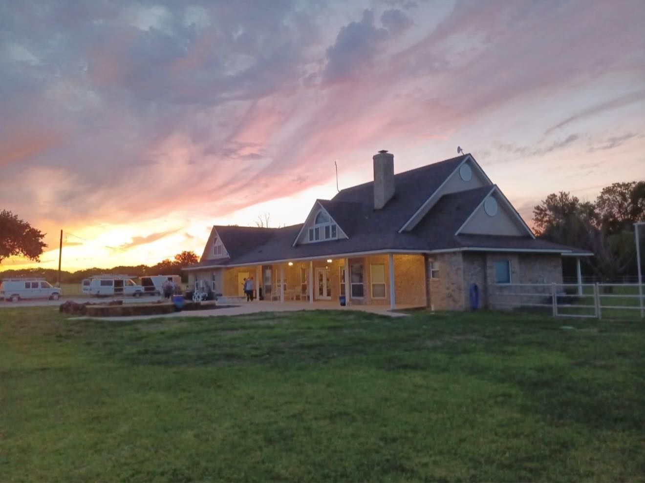 House at sunset with glowing porch lights and a pink sky over a grassy yard