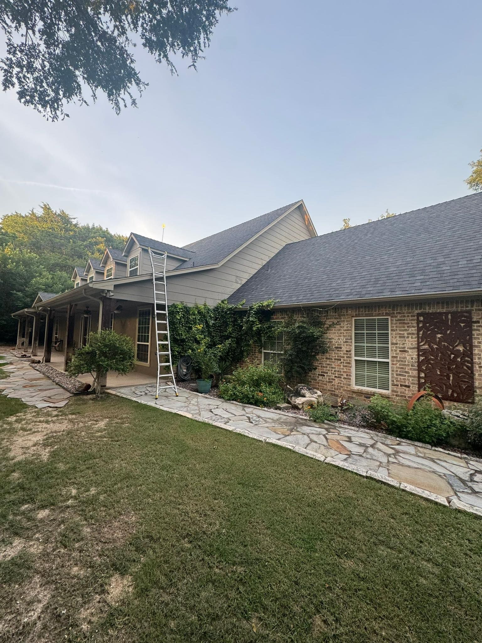 Stone house with a dark roof, ivy-covered wall, ladder, and a grassy yard at dusk