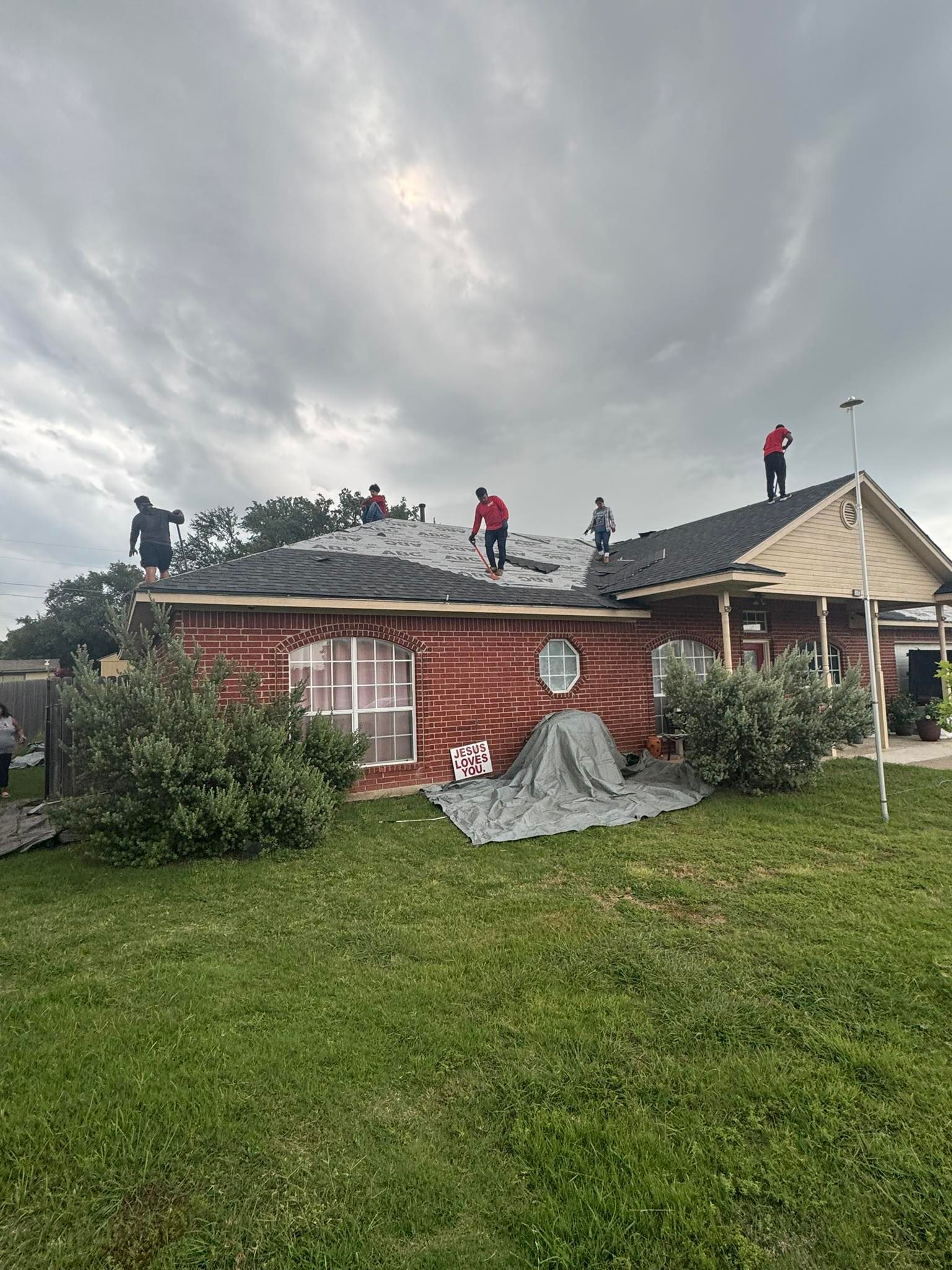 People on a damaged roof after a storm, with debris on a lawn and cloudy sky.