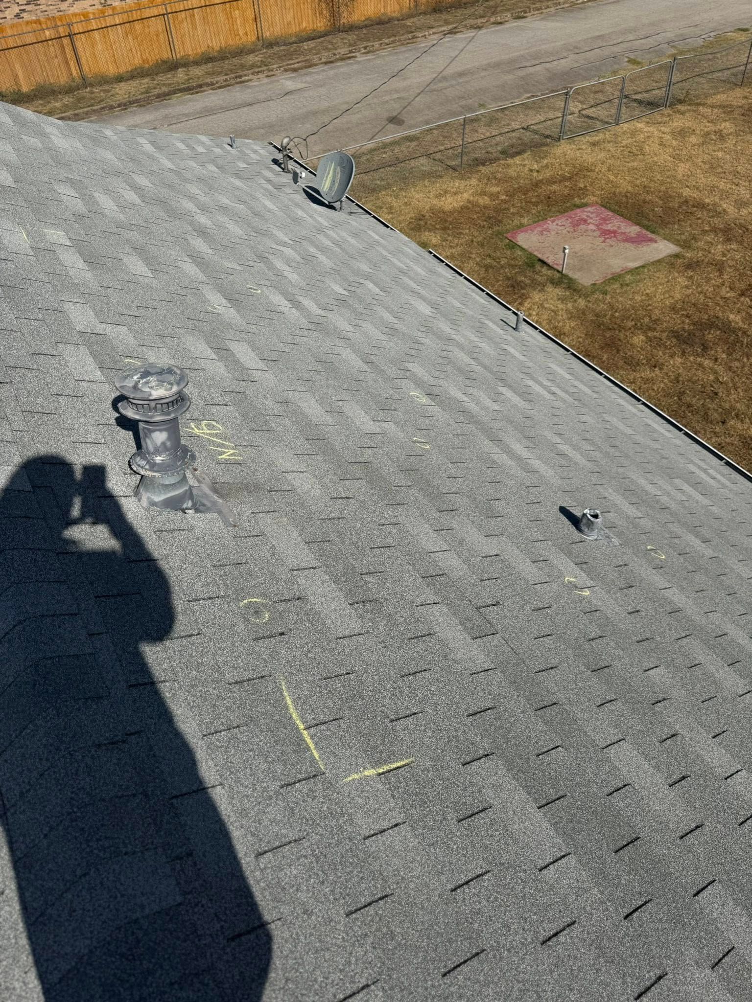 Shingled rooftop with vents, a shadow, and a grassy yard in the background