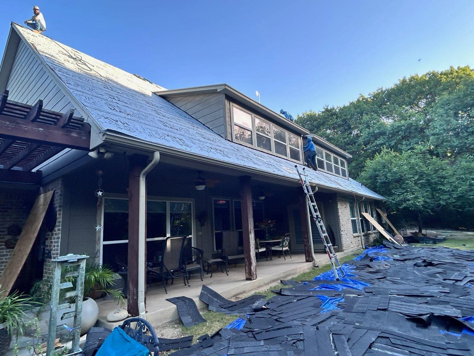 Traditional wooden house with a steep roof, partially covered in blue tarps under a clear sky