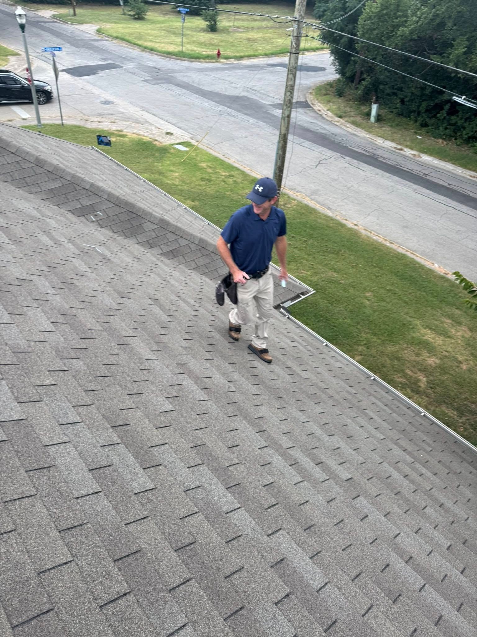 Person in a navy shirt and khaki pants walking on a shingled roof near a street.