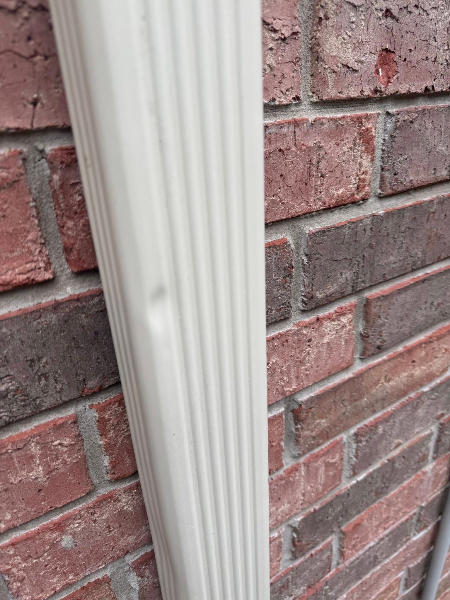 White vertical downspout against a red brick wall