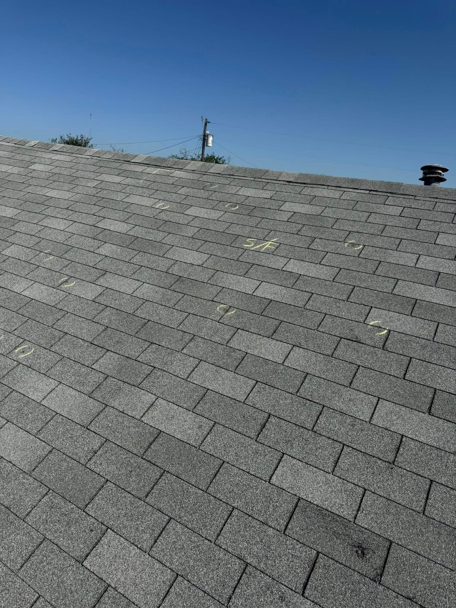 Gray shingled roof with two vent pipes under a clear blue sky