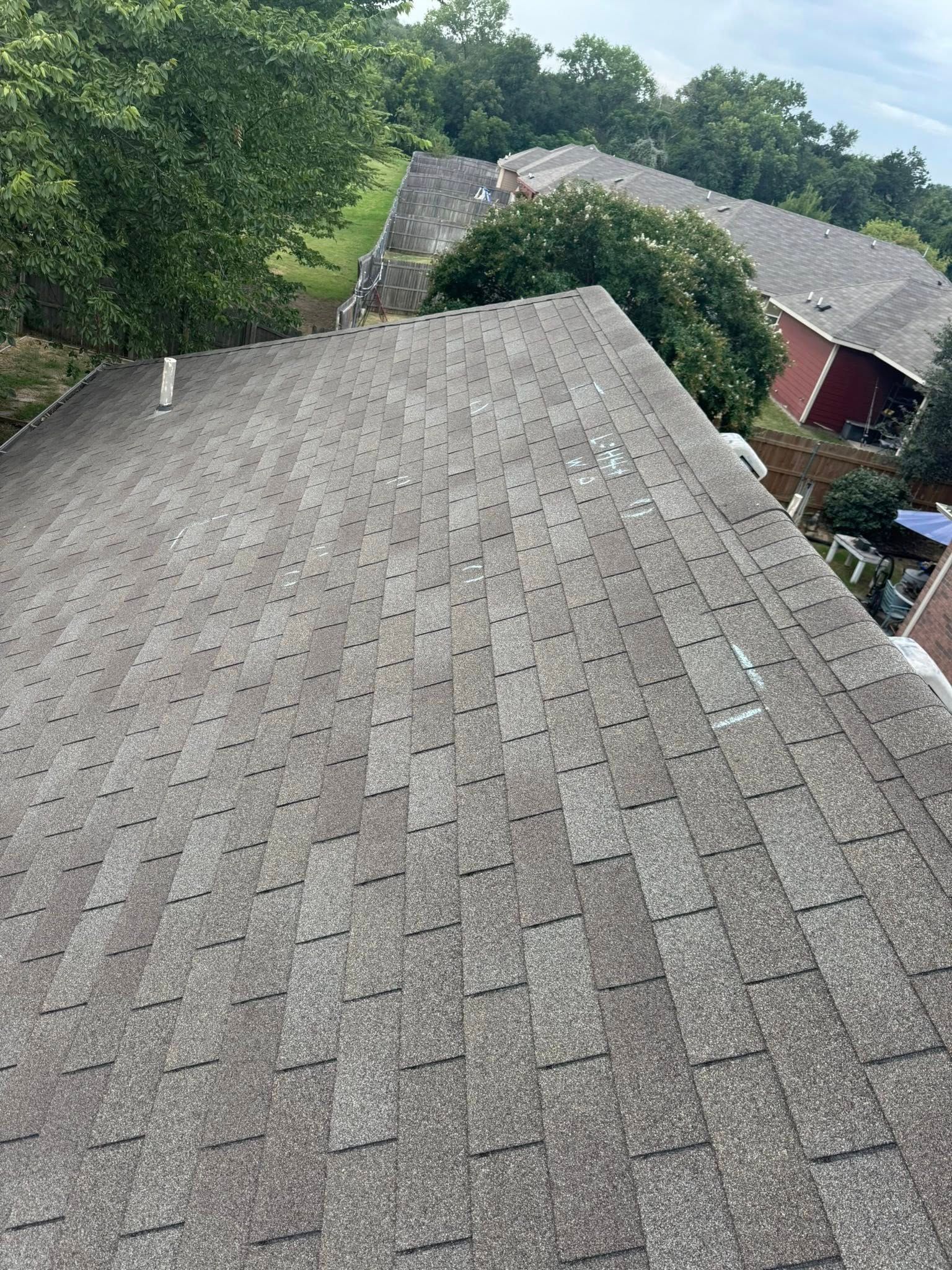 Gray shingled rooftop overlooking trees and neighboring houses