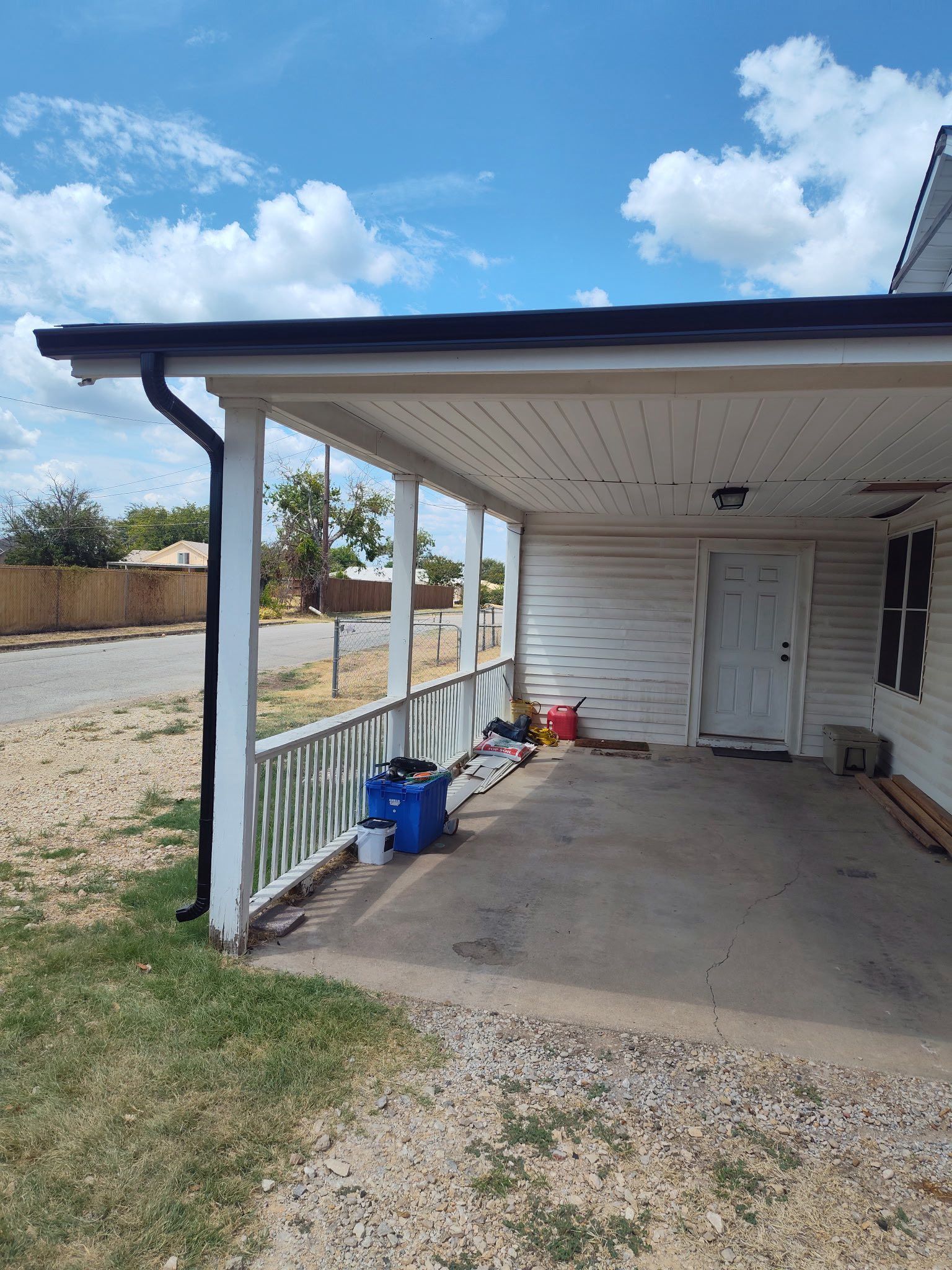 Covered front porch with white posts, blue trim, concrete floor, and yard view under a cloudy sky