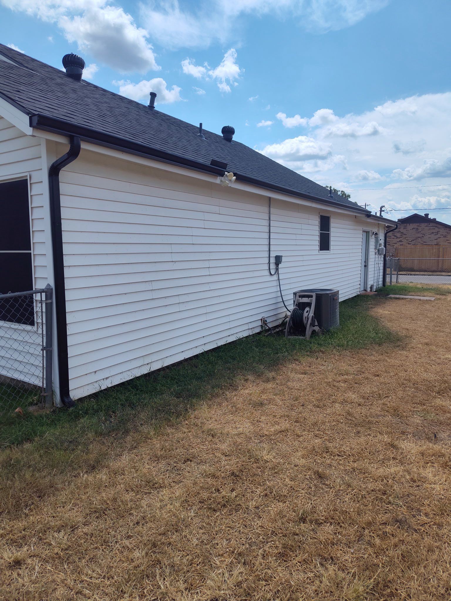 White house siding with dark roof beside a grassy yard under a partly cloudy sky.