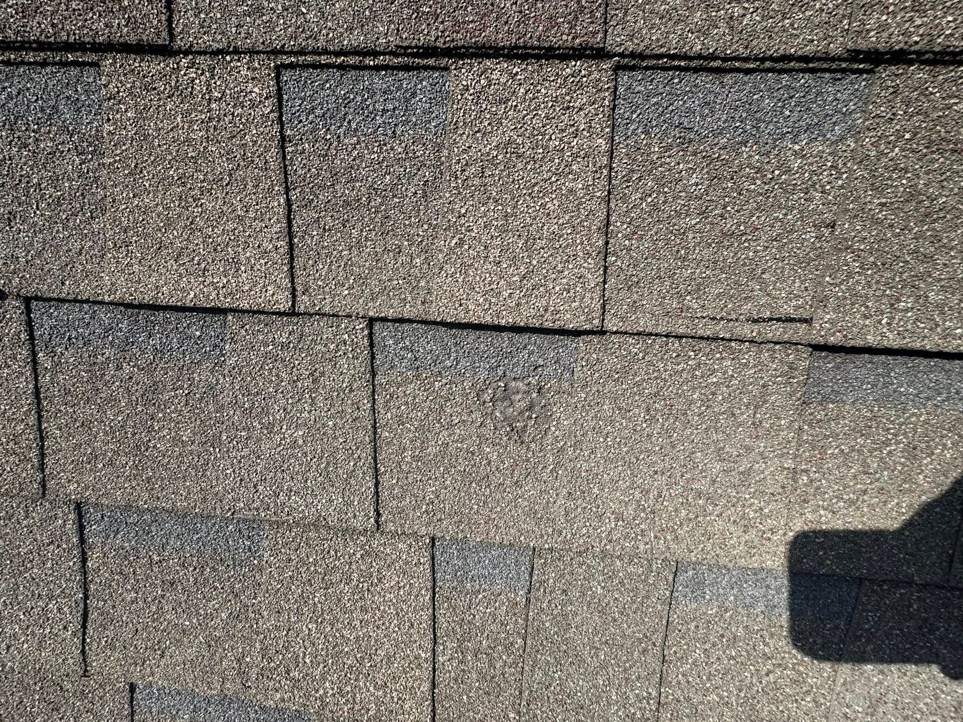 Close-up of gray asphalt roof shingles with a dark shadow at the lower right