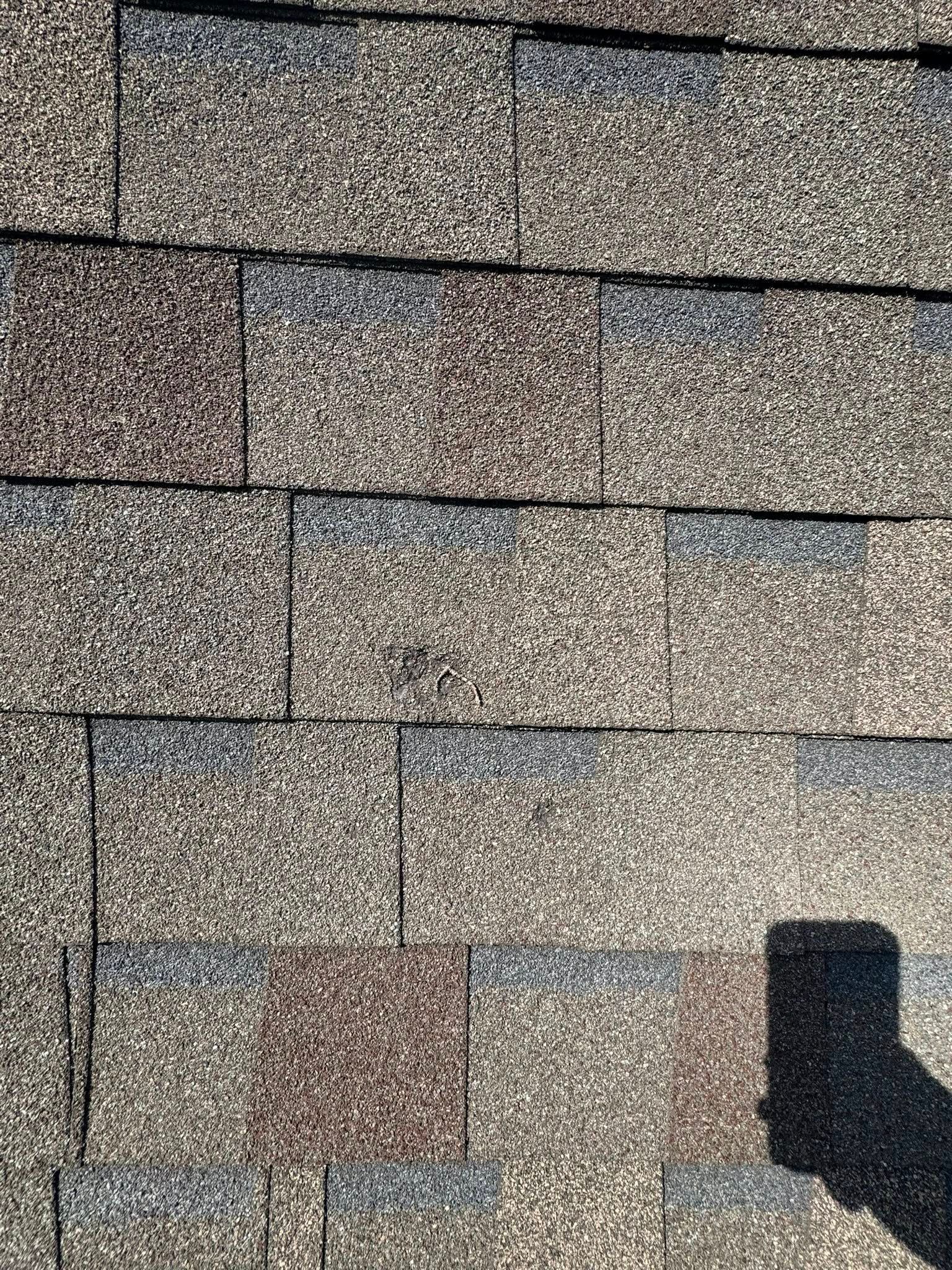 Close-up of brown asphalt roof shingles with a dark shadow in the lower right corner