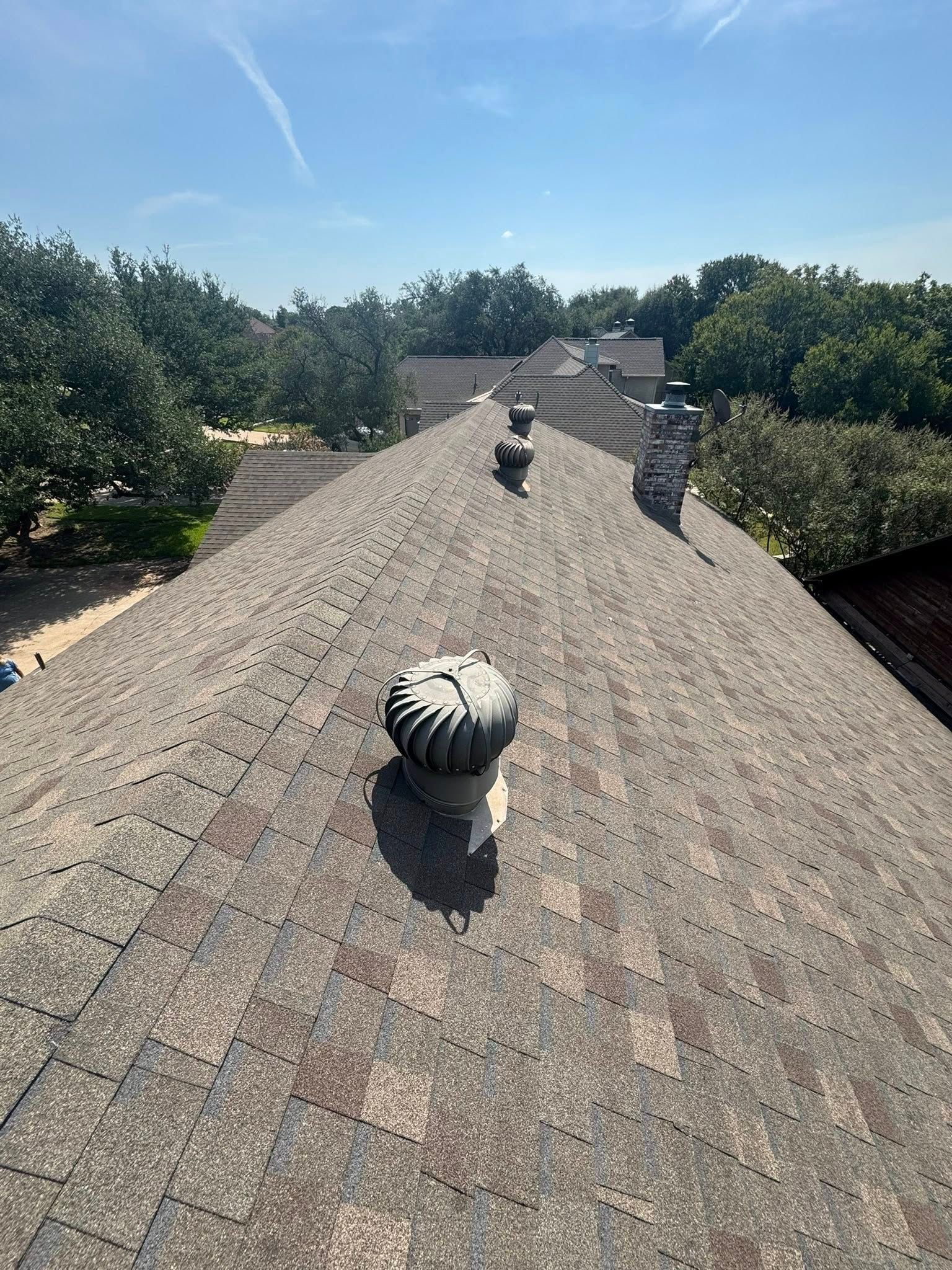 Shingle rooftop with vents, viewed from above, with trees and blue sky in the background