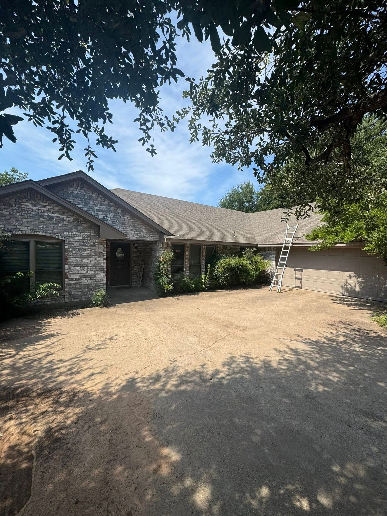 Stone house with a gabled roof, shaded front courtyard, and trees overhead