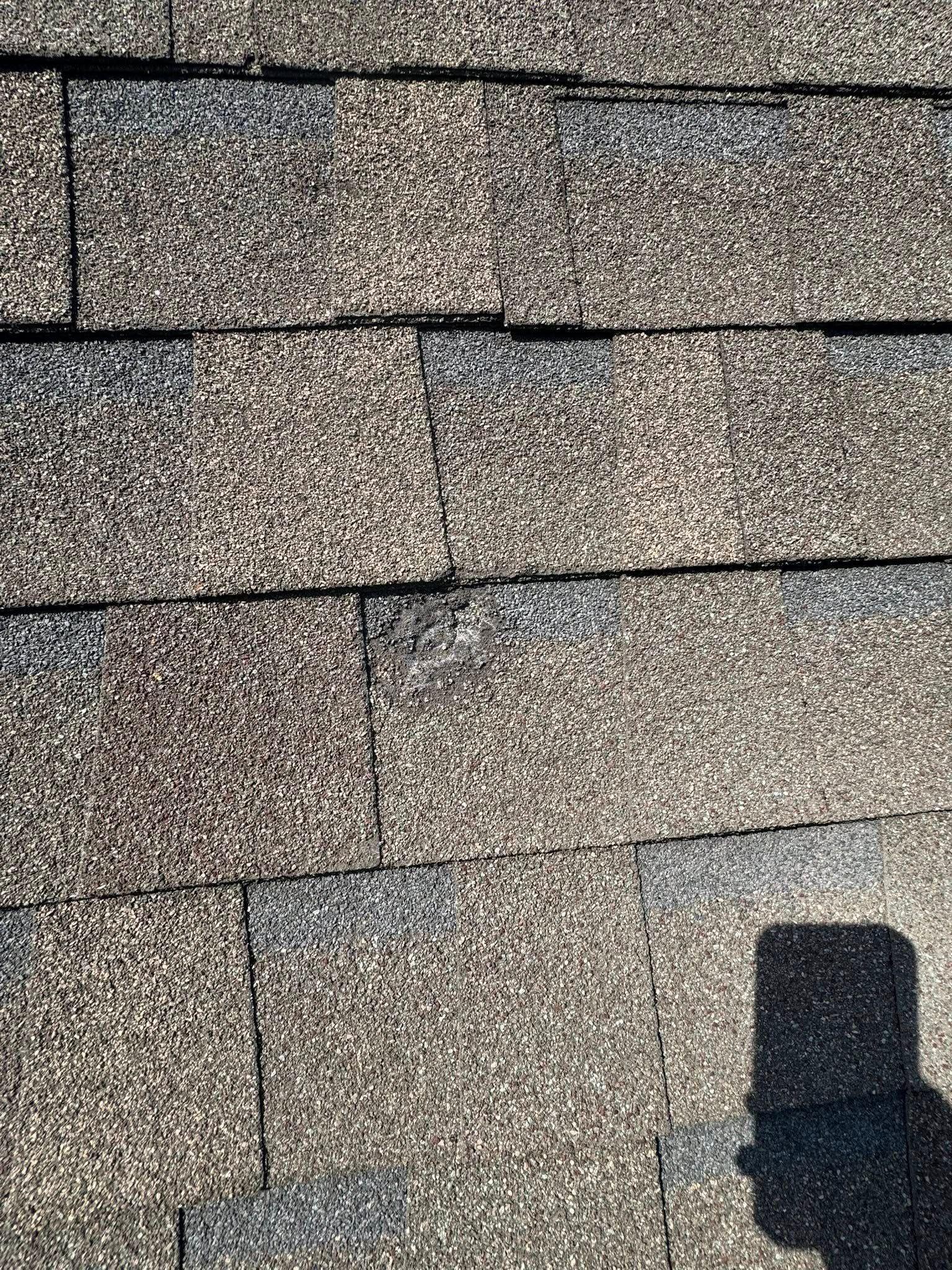 Close-up of gray roof shingles with a dark chimney shadow in the lower right.