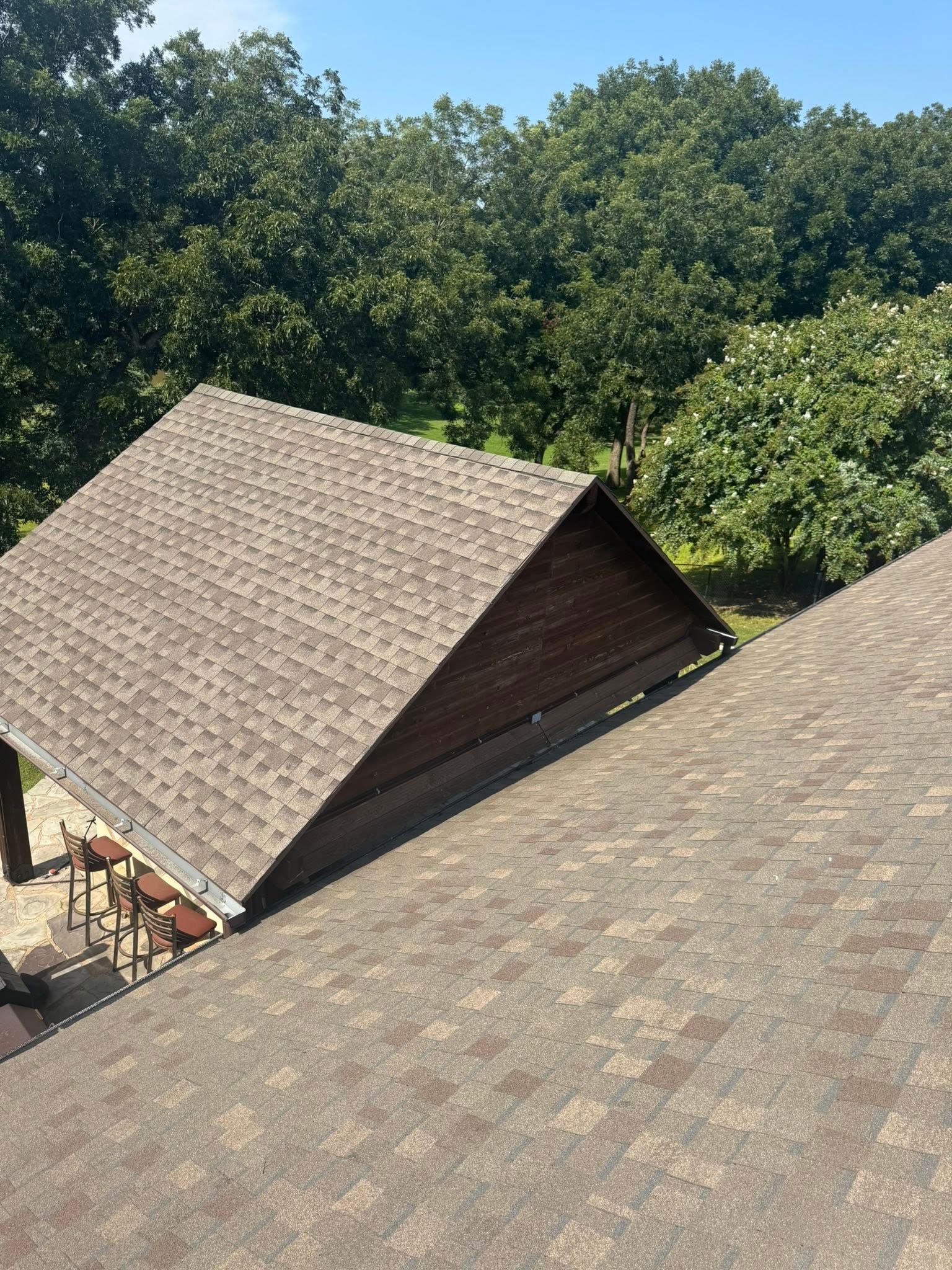 Shingled rooftops of a wooden building beside dense green trees on a sunny day