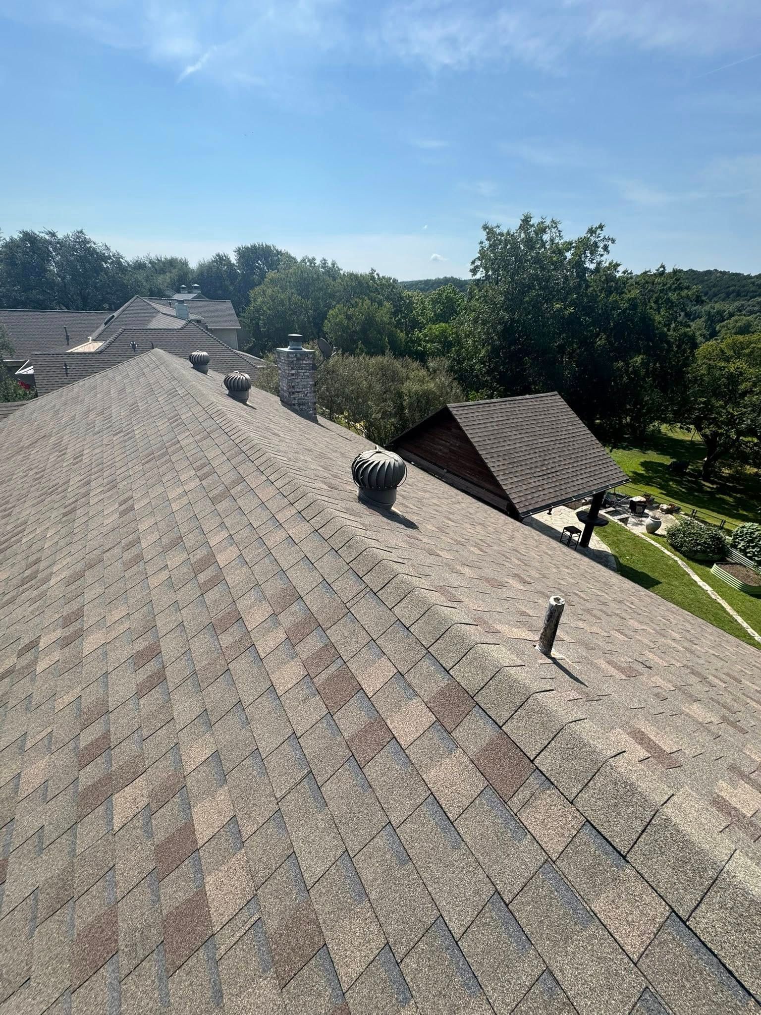 Roof shingles and vents on a house under a clear blue sky, with trees in the background