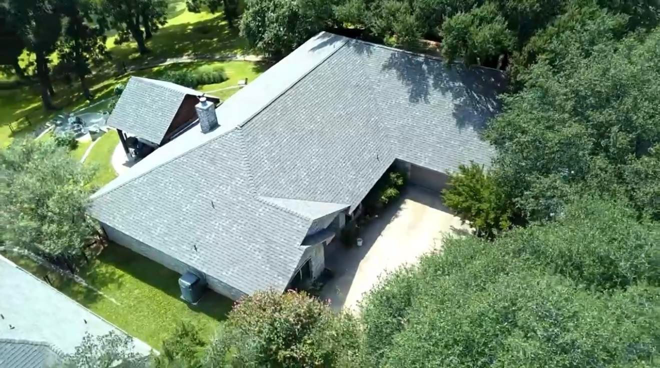 Aerial view of a house with a gray roof surrounded by dense green trees and vegetation