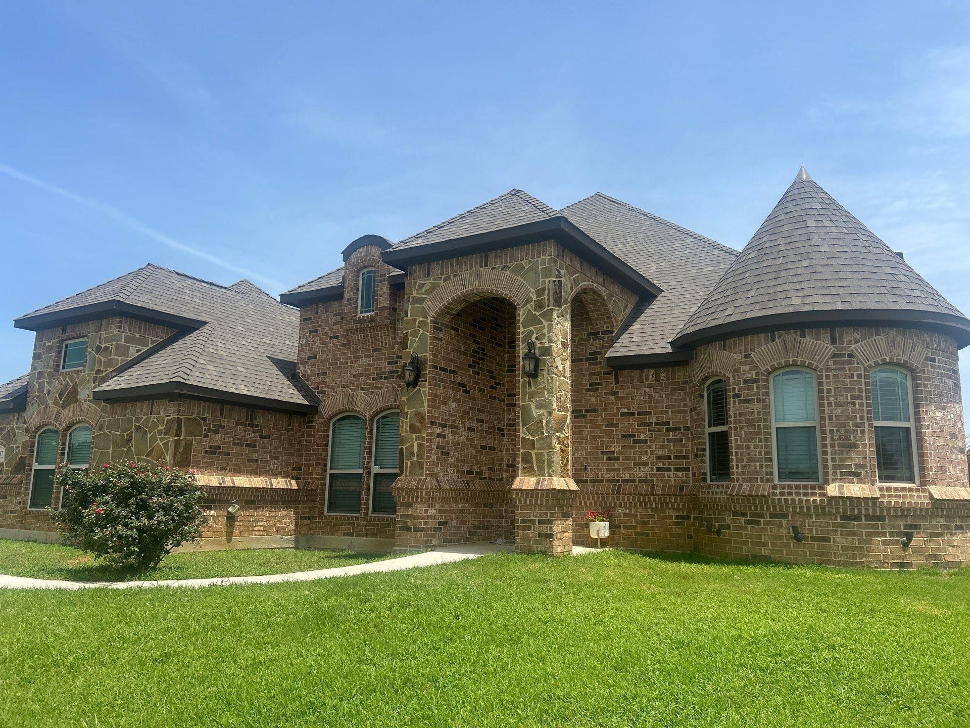Brick house with arched entry, turret-style rooflines, and a green lawn under a clear sky