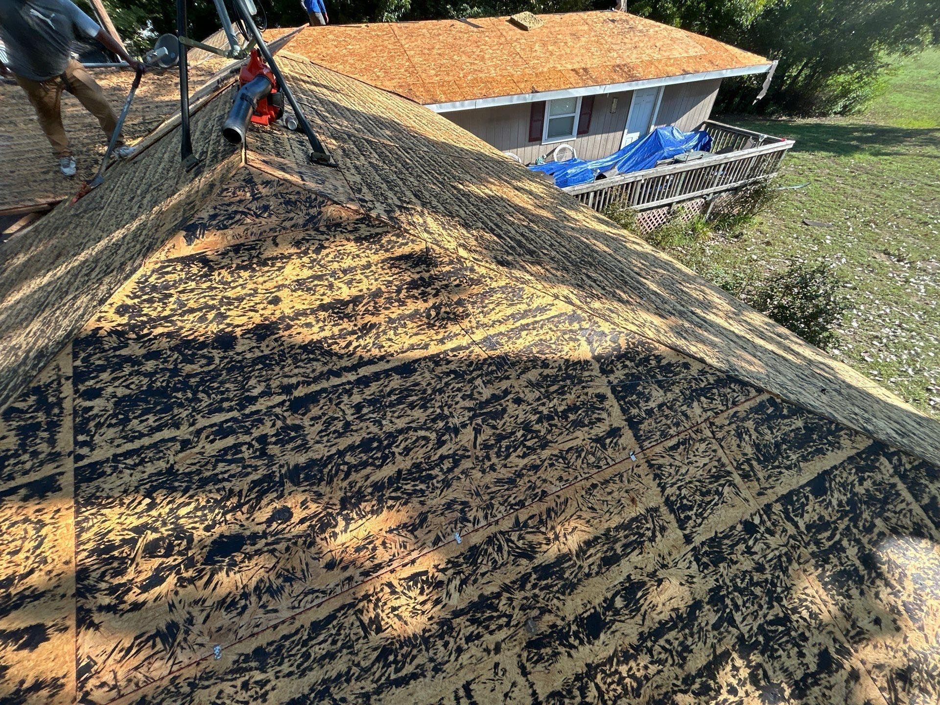 Aerial view of a roof covered in dark debris, with a house and yard in the background.