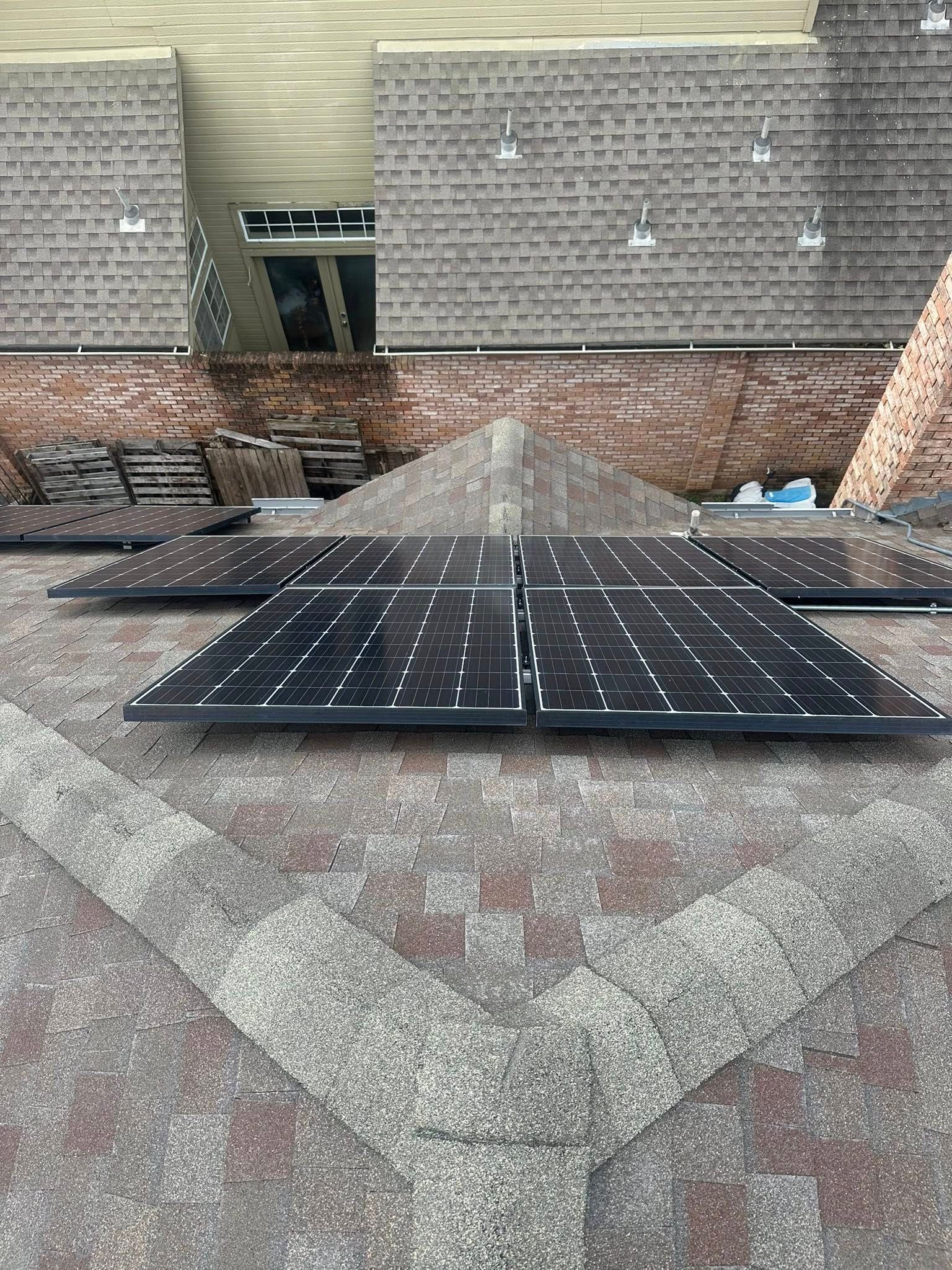 Two black solar panels mounted on a sloped shingled rooftop beside brick buildings.