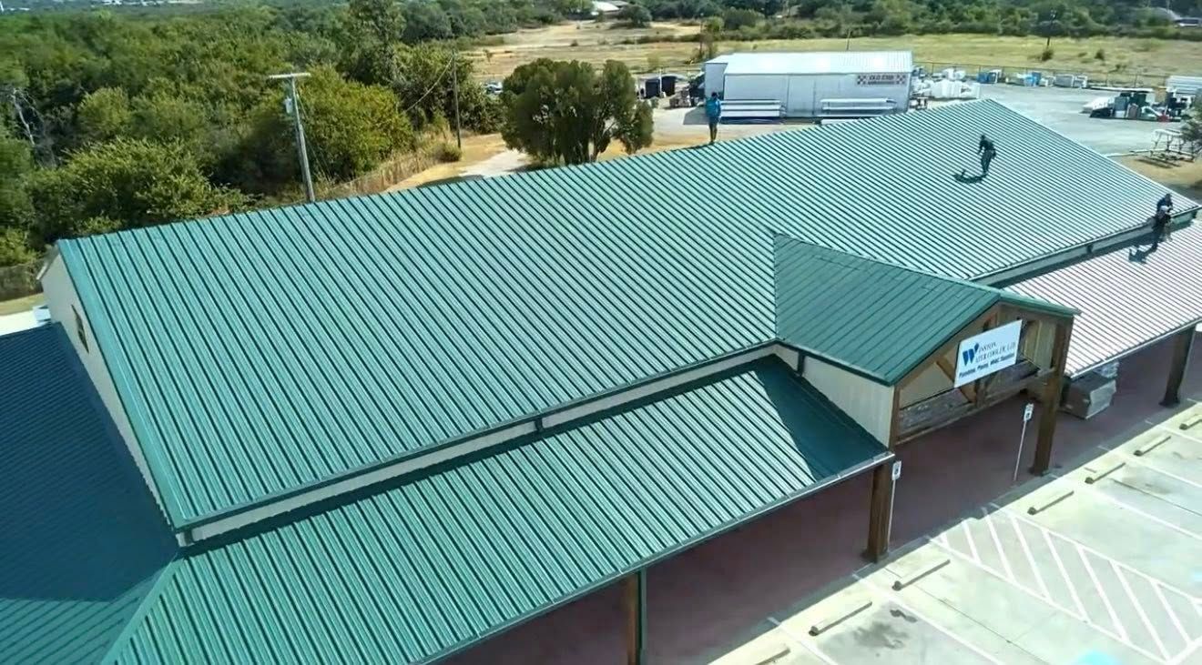 Aerial view of a teal-roofed building in a rural area with trees and open land nearby