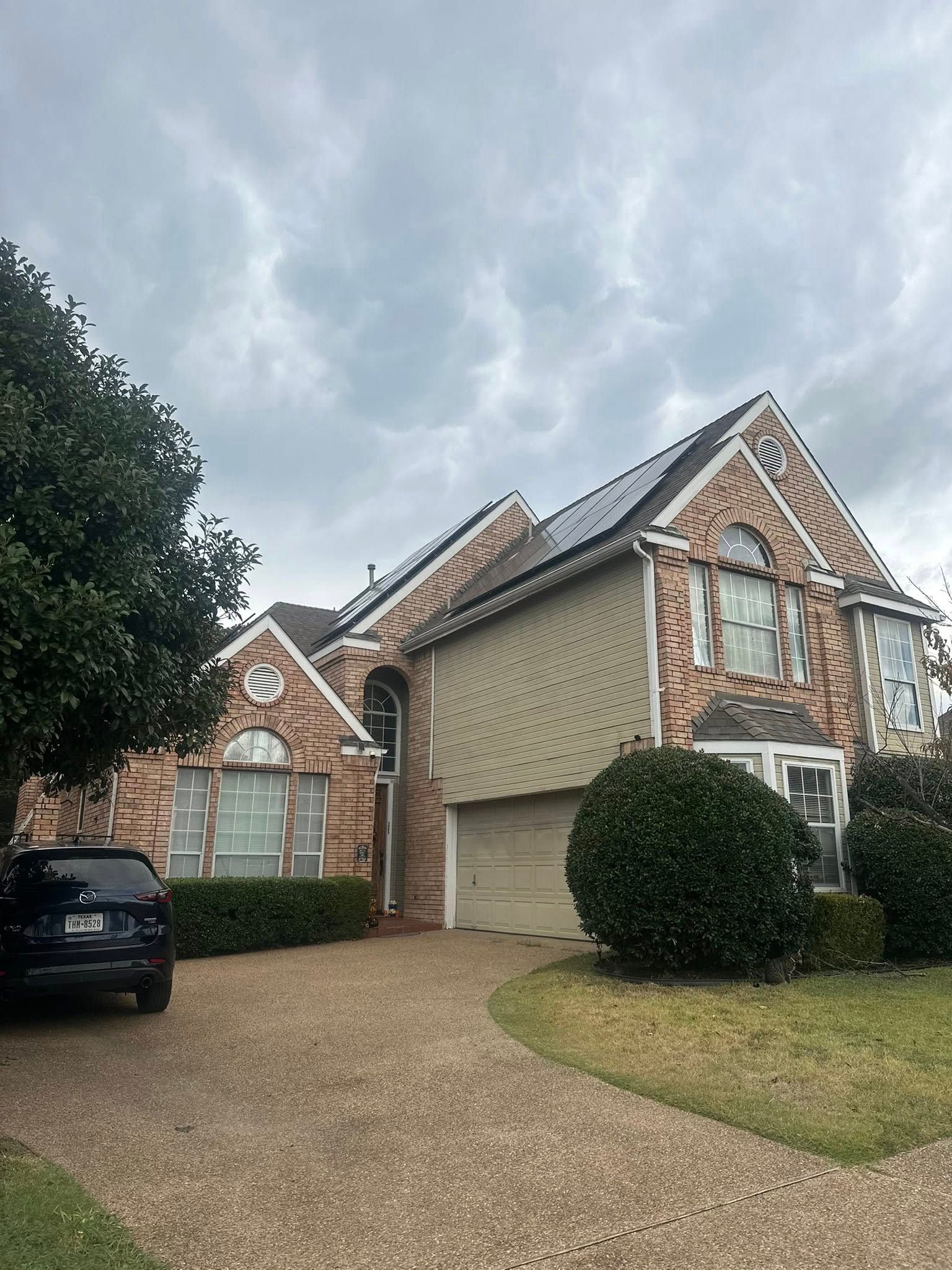 Suburban brick house with a double garage, gravel driveway, parked car, and cloudy sky