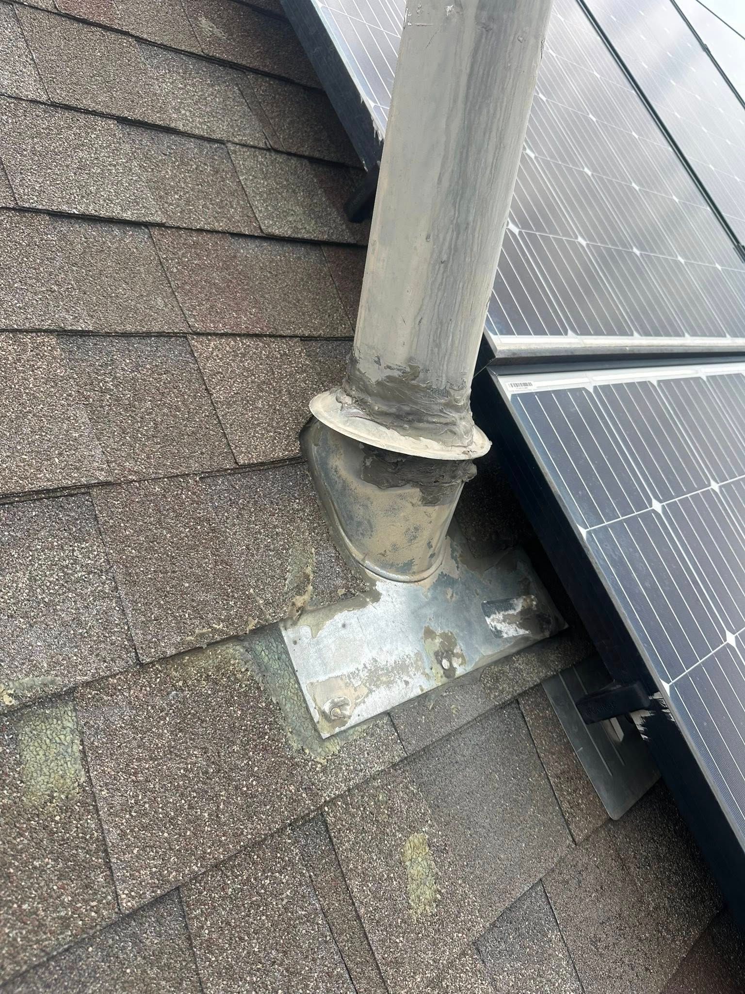 Roof vent pipe with damaged flashing on asphalt shingles beside solar panels