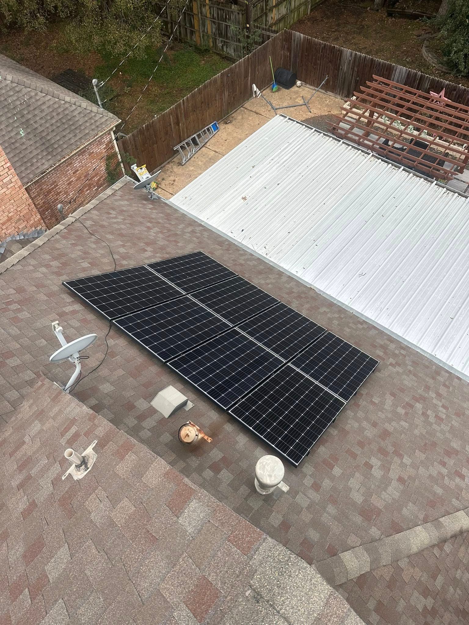 Rooftop solar panel installation with black and white panels on a flat roof near trees and brick buildings