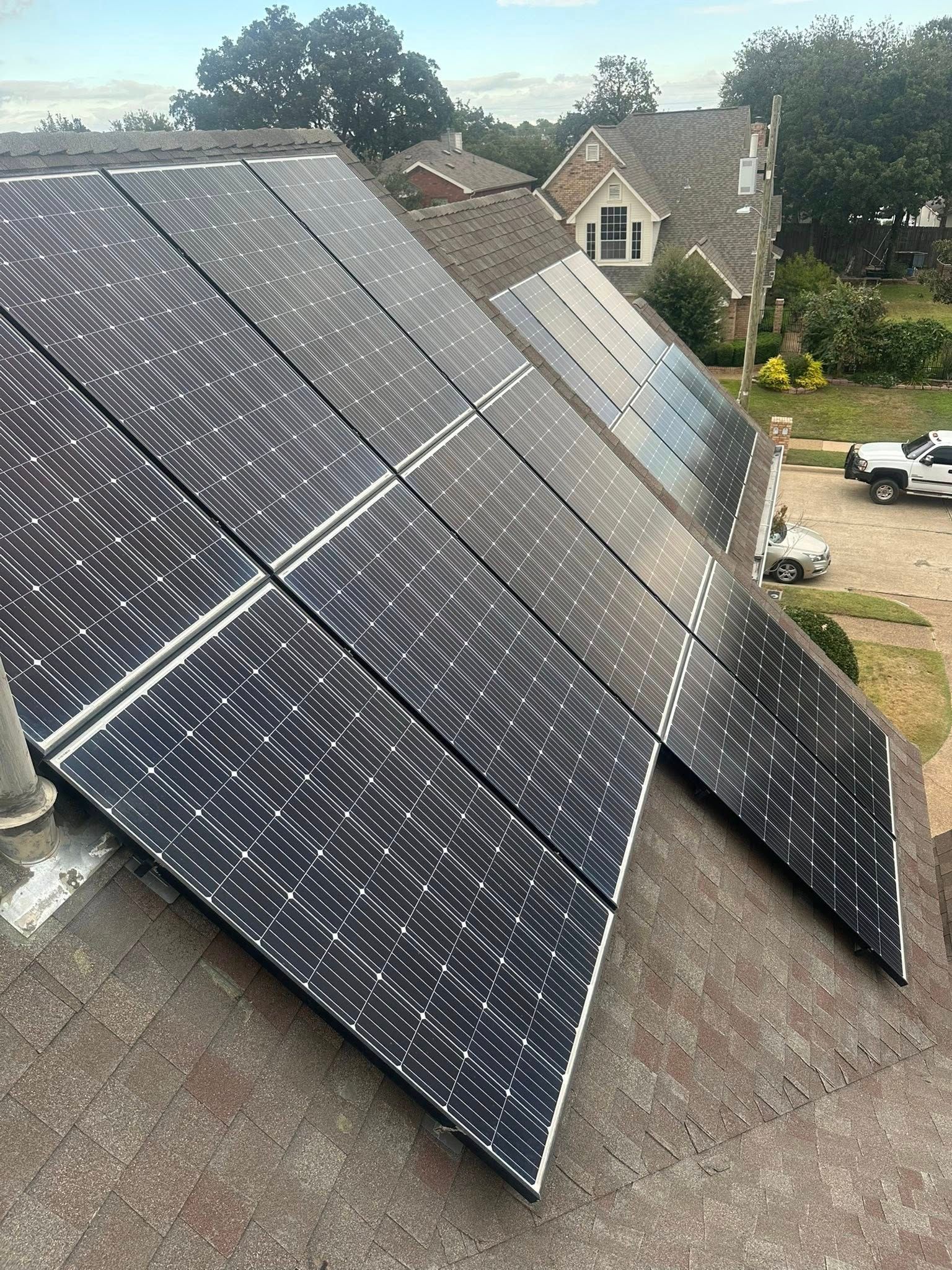 Large solar panel array mounted on a rooftop, with houses and trees in the background.