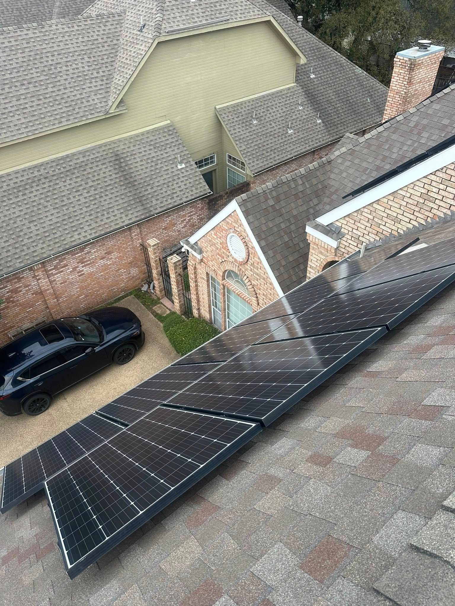 Rooftop solar panels on a slanted roof above a residential neighborhood with parked cars.