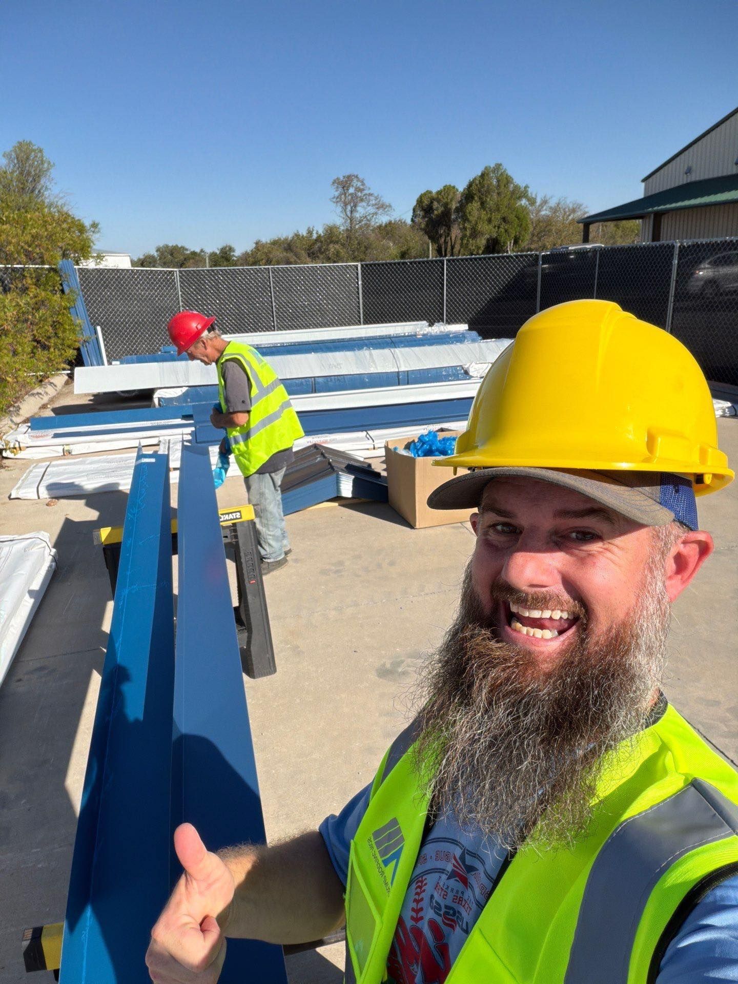 Construction workers in hard hats and safety vests handling blue materials outdoors, one smiling at camera