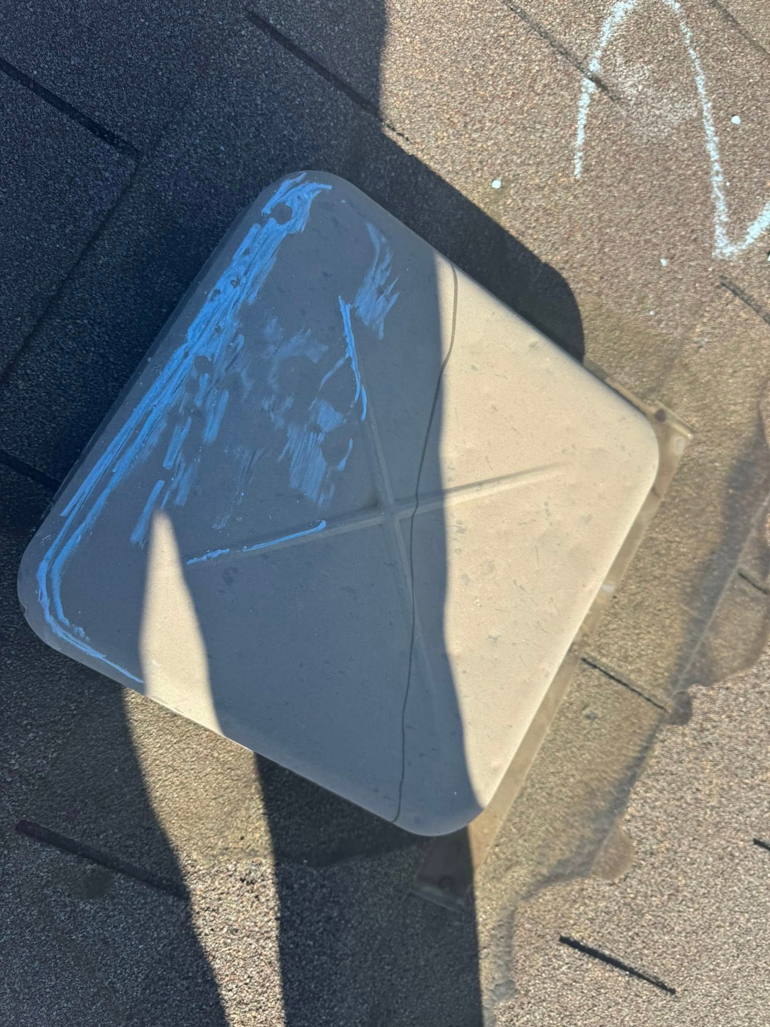 White rooftop vent with blue paint marks on dark shingles in sunlight
