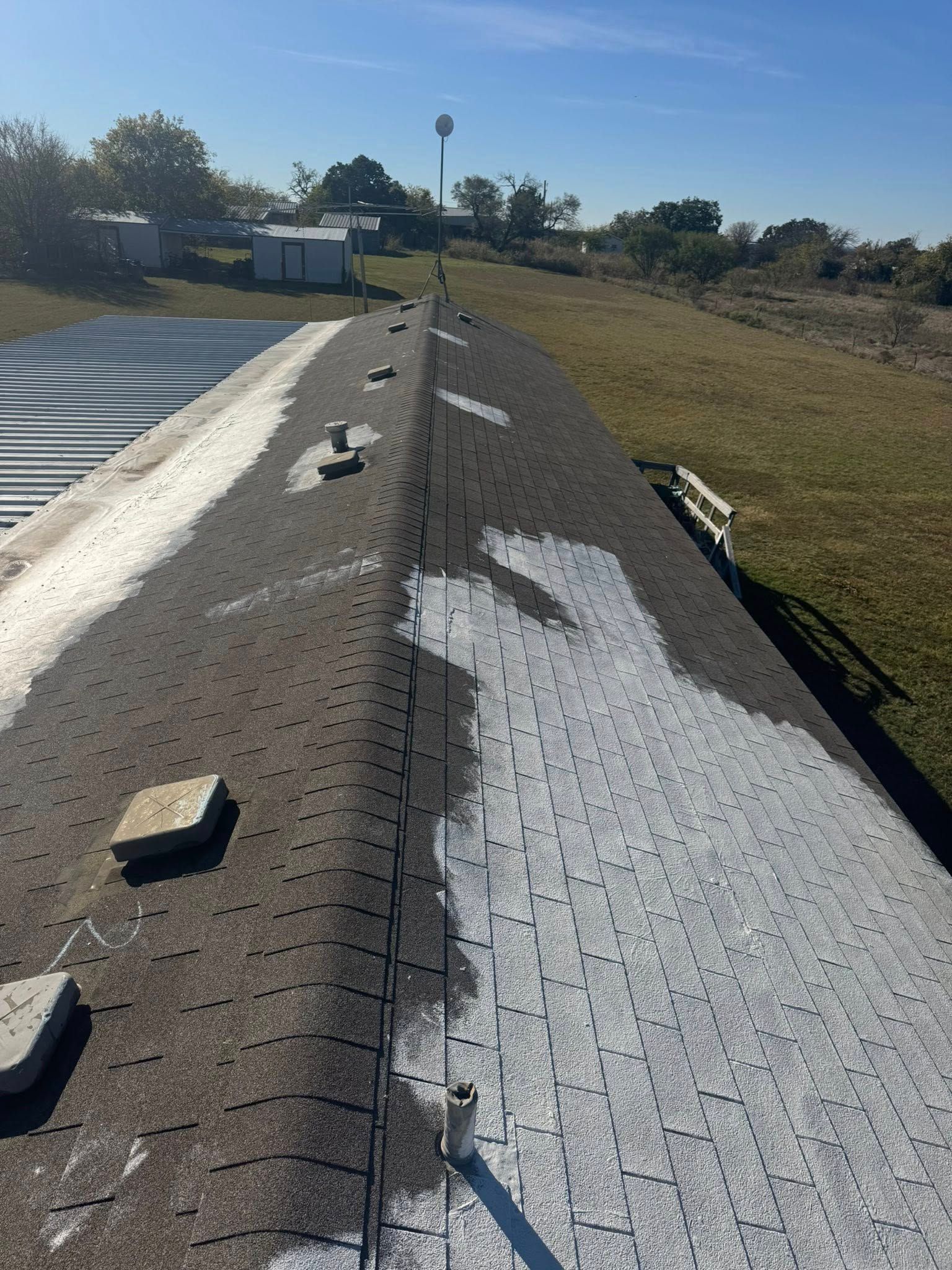 Rooftop with a central seam, white coating, and loose bricks under a sunny sky