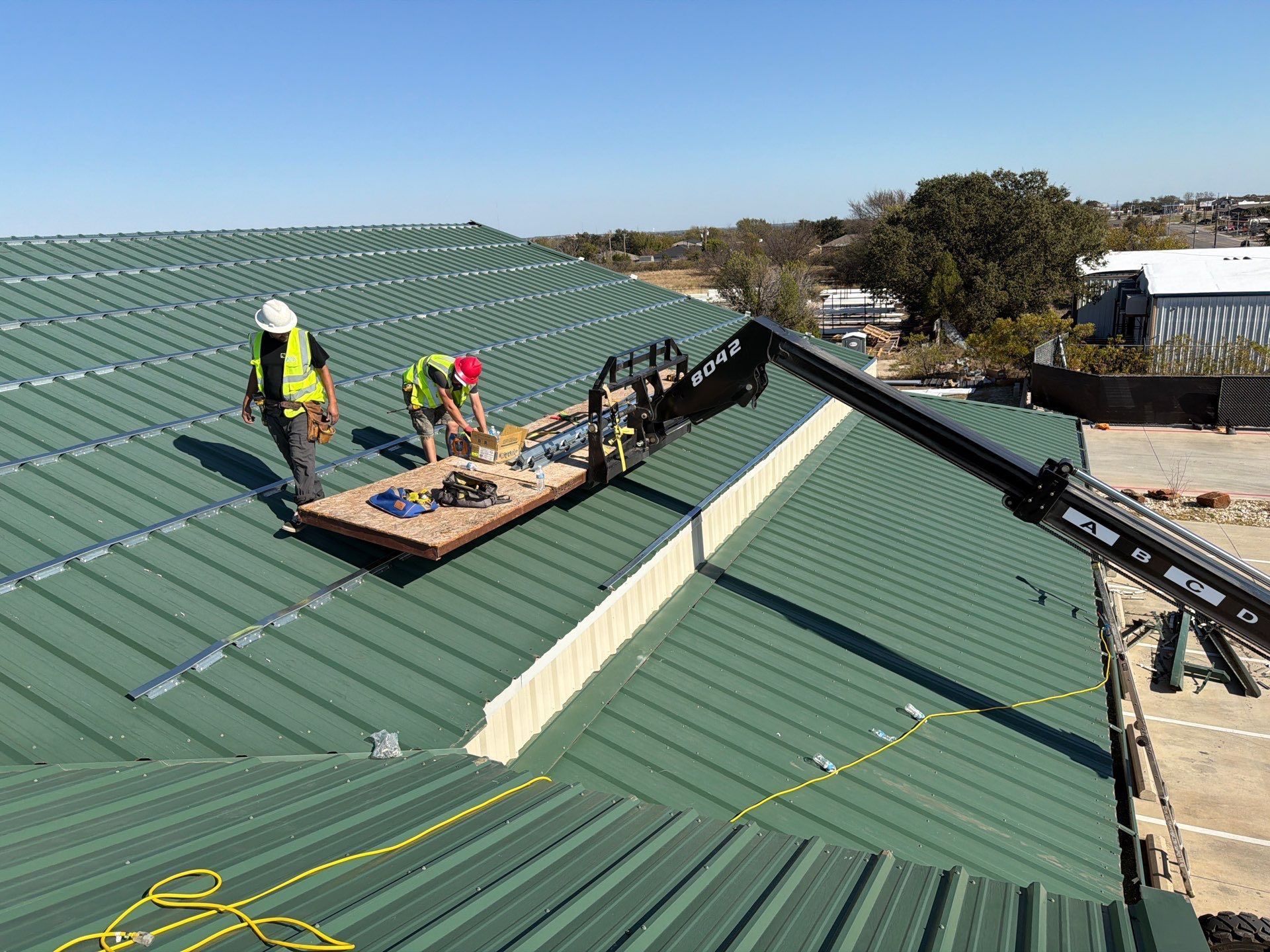 Workers installing solar panels on a green metal roof with a suspended platform.