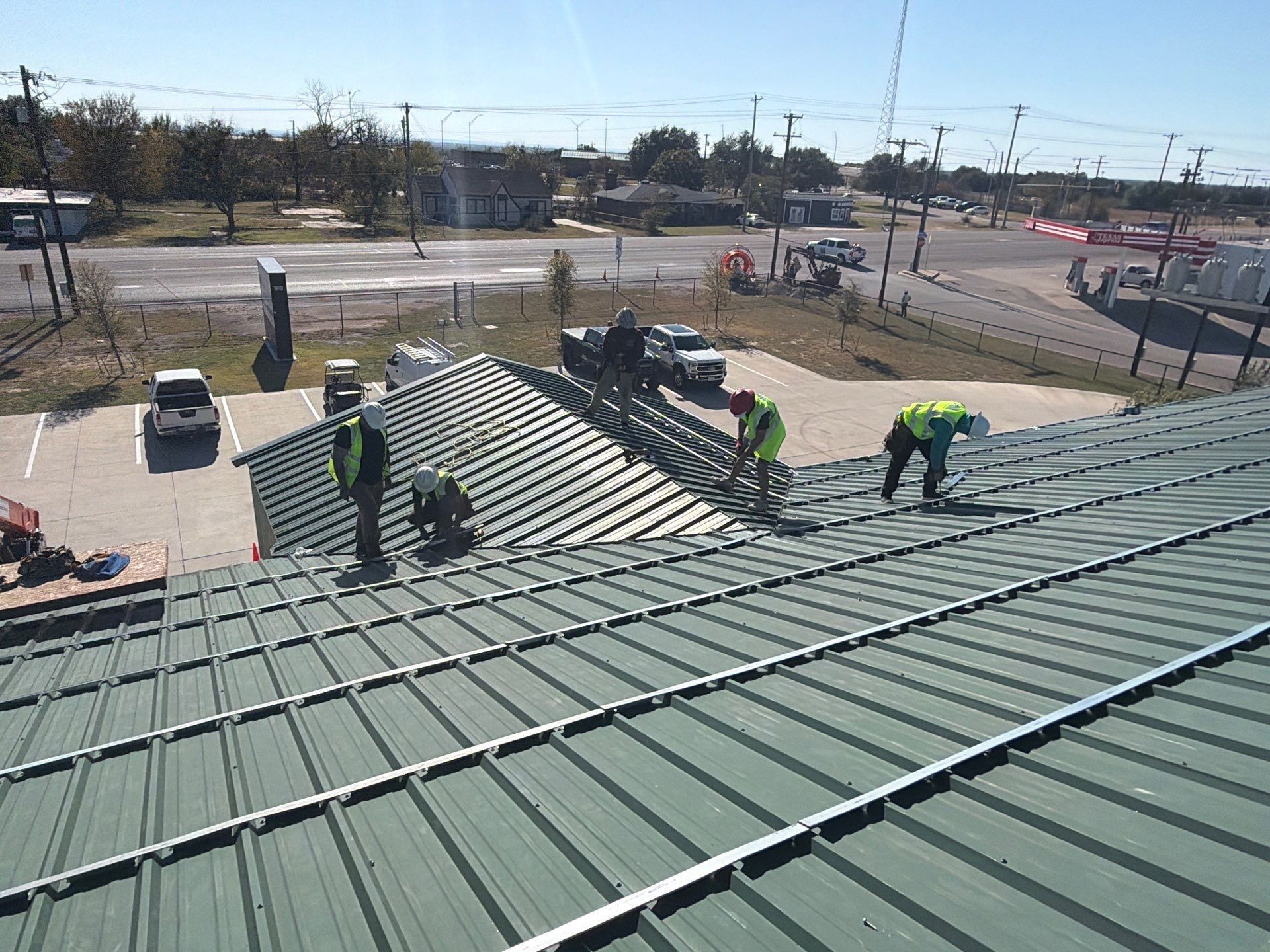 Workers in neon vests installing green metal roofing on a large sloped roof outdoors.