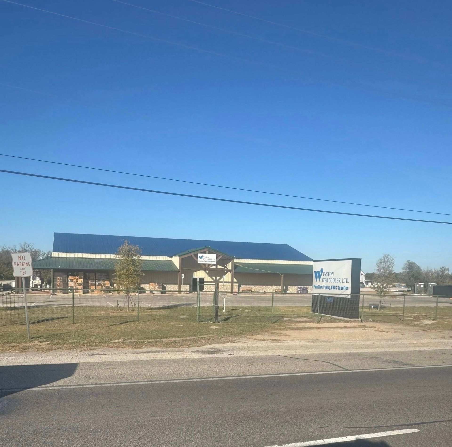 Roadside building with a blue roof behind a fence, with a sign in front under a clear sky.