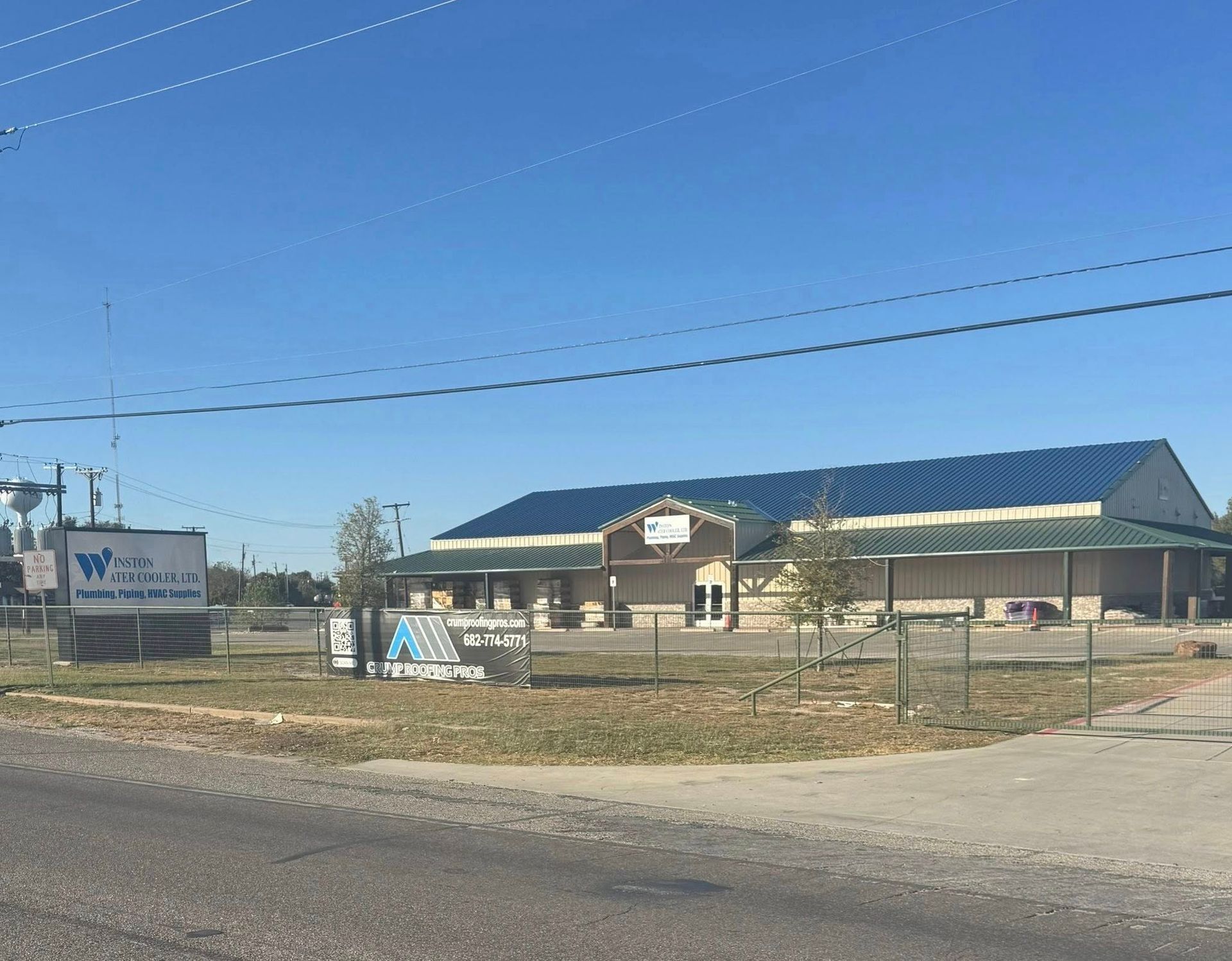 Rural roadside business with a blue-roofed building, fenced yard, and sign under a clear sky.