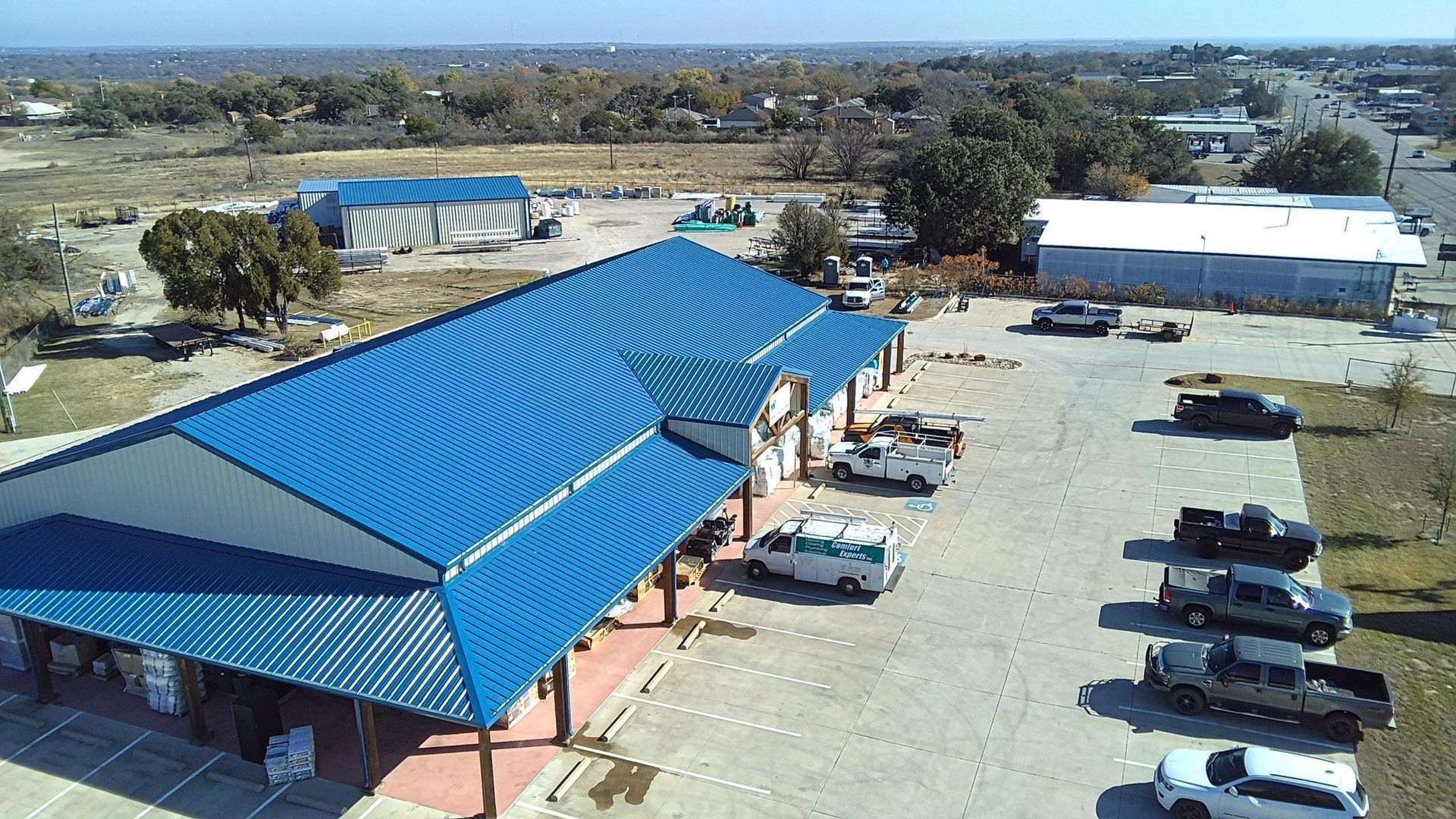 Aerial view of a blue-roofed building with parked cars in a paved lot.