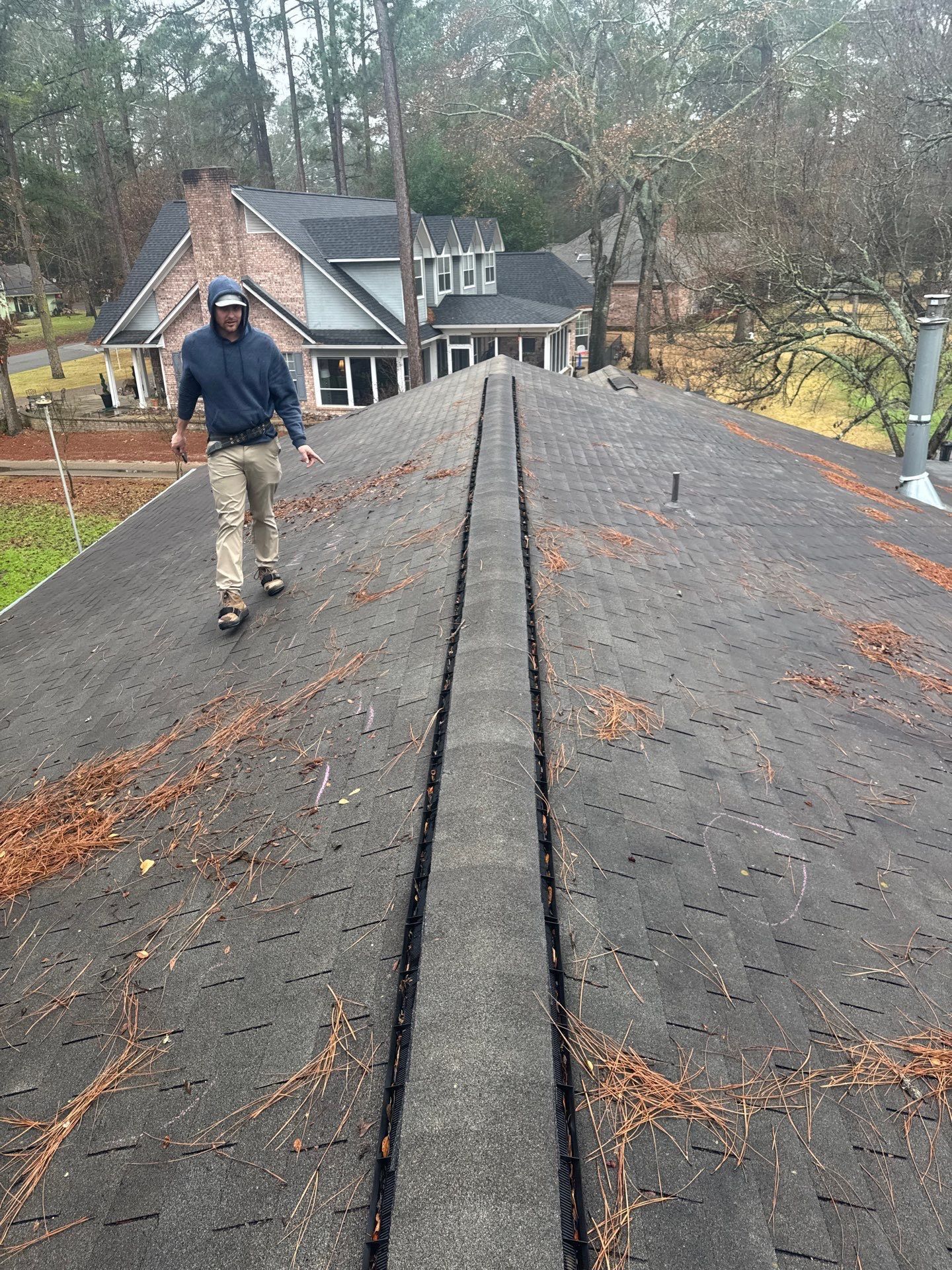 Worker walking on a steep shingled roof with trees and houses in the background