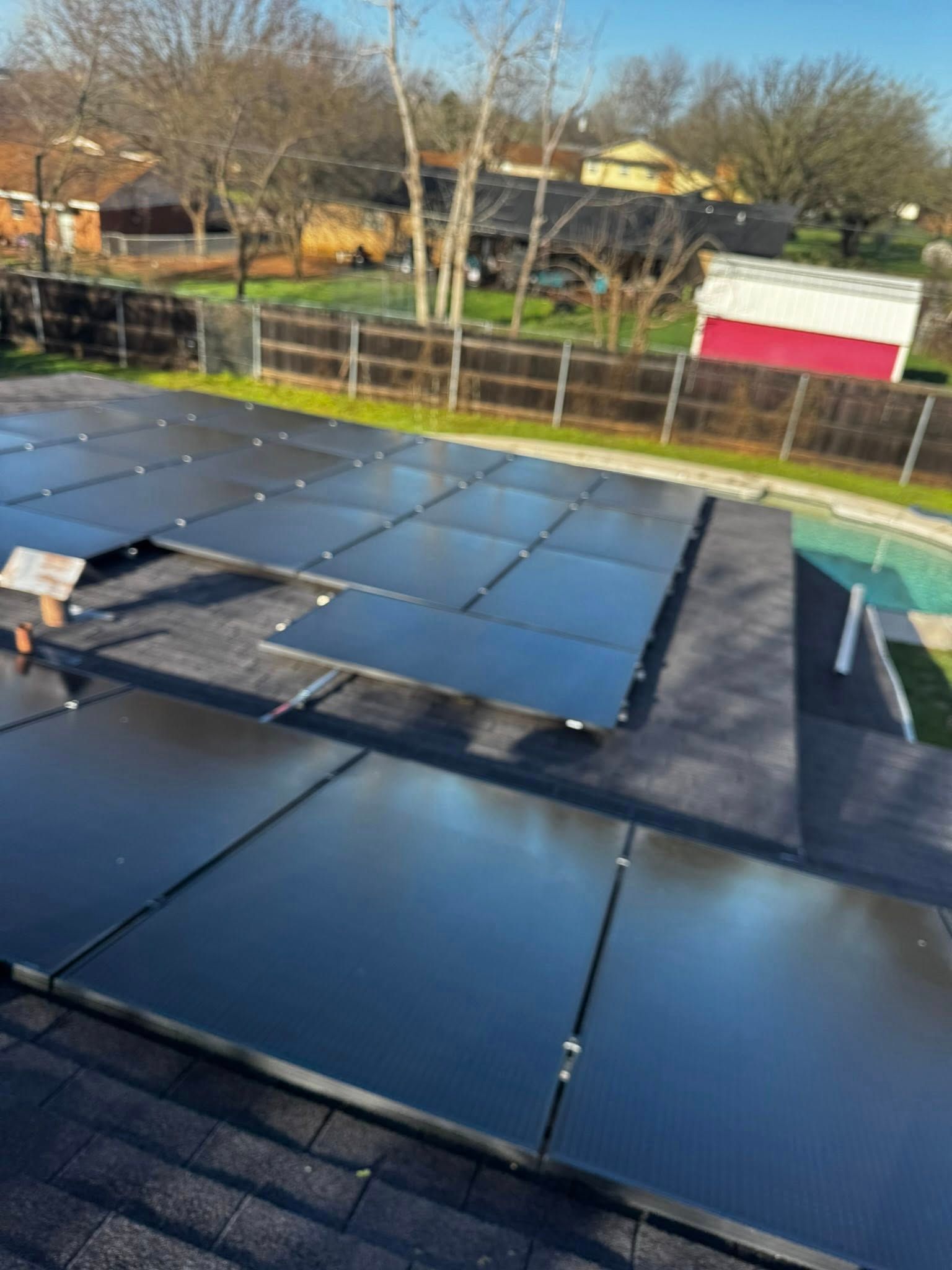 Solar panels arranged on a rooftop under a clear sky, with trees and houses in the background