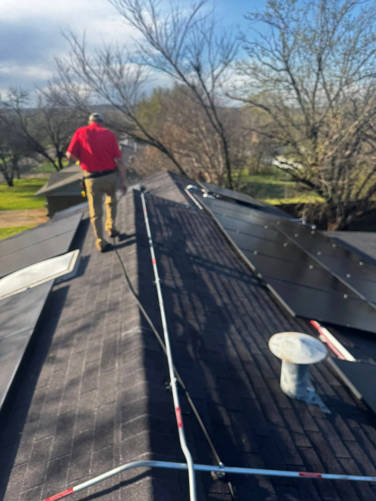 Worker in red jacket on a rooftop, installing black roofing under bright daylight.