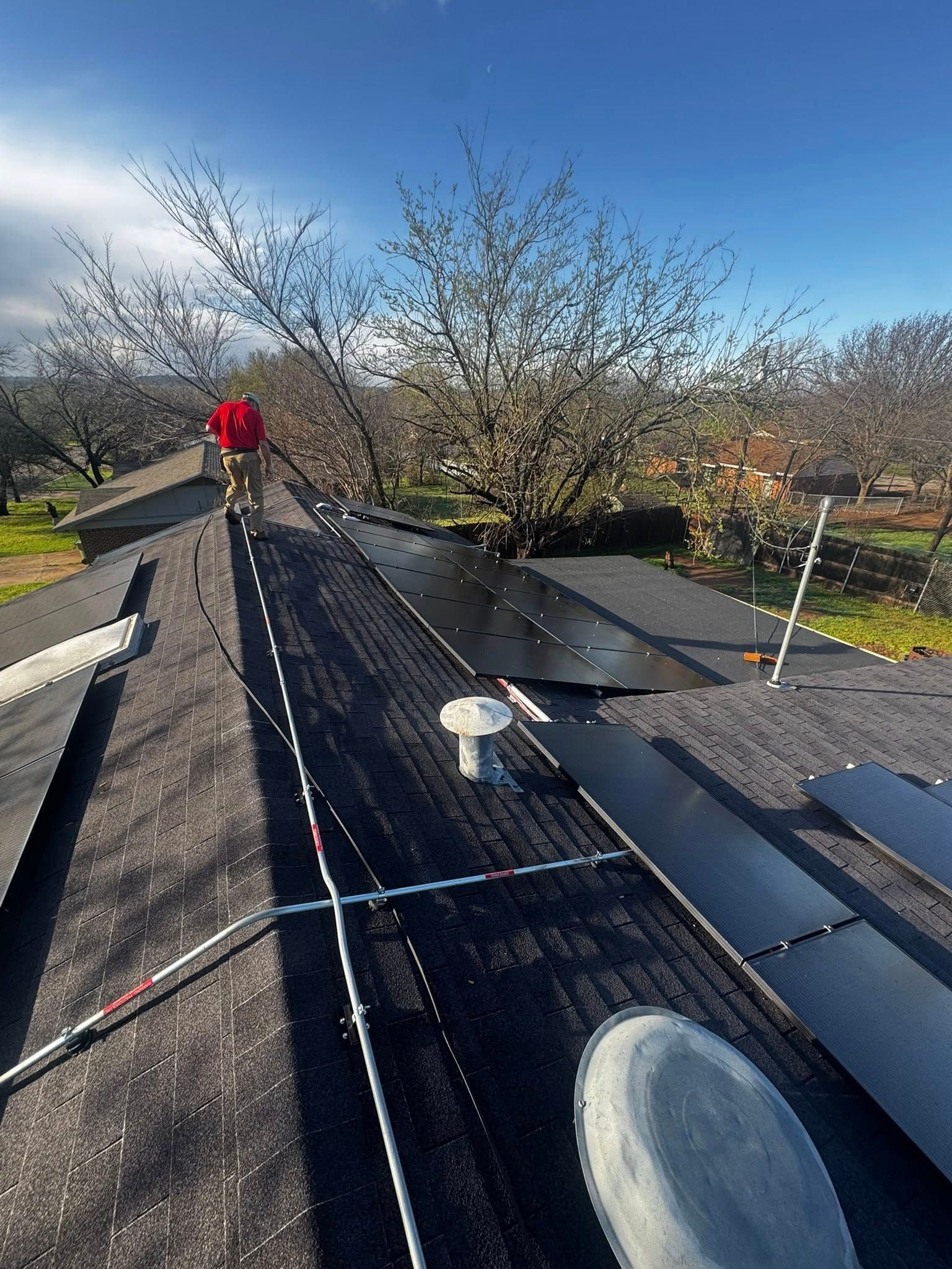 Roof with solar panels and a worker in a red jacket adjusting equipment under a blue sky