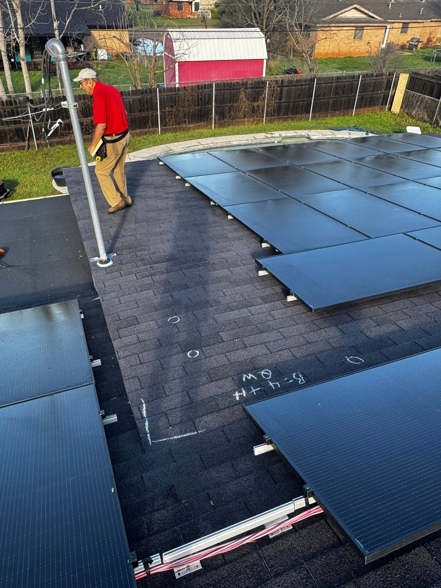Worker installing blue solar panels on a rooftop, with a residential neighborhood in the background.