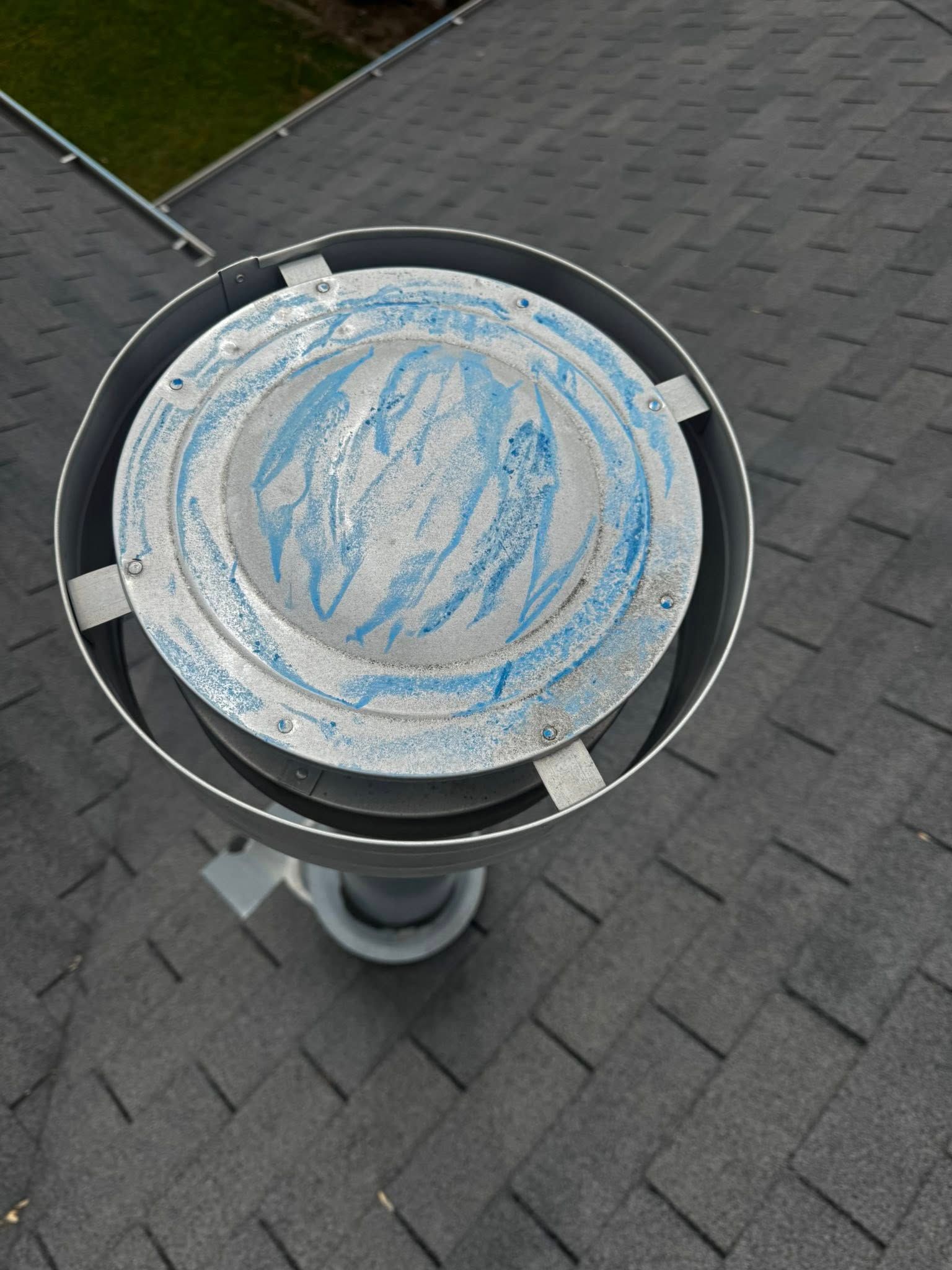Round rooftop vent or dish with blue-and-white paint on a gray shingled roof
