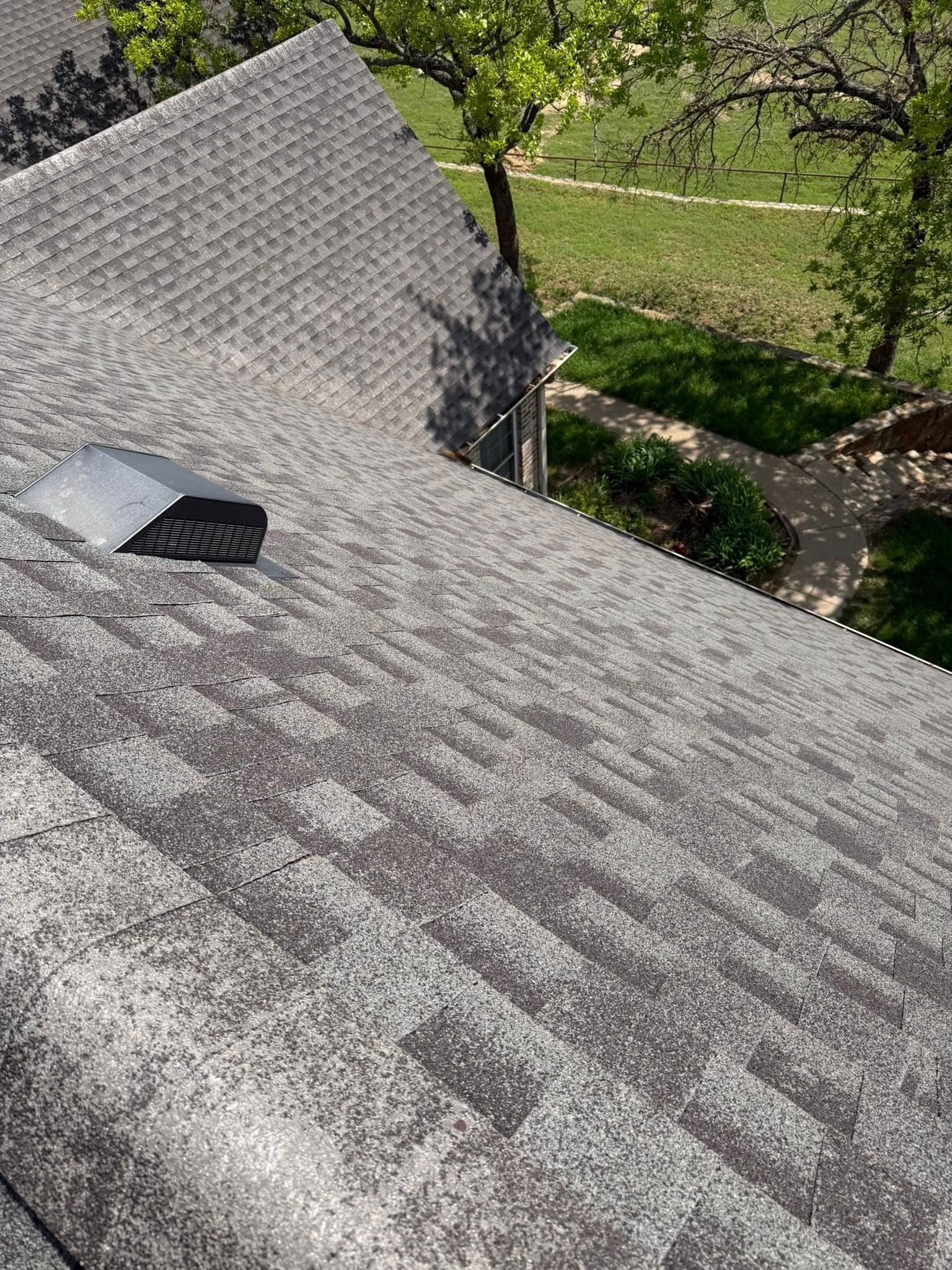 Shingled roof with a small skylight and a vent, viewed from above with trees and a yard below