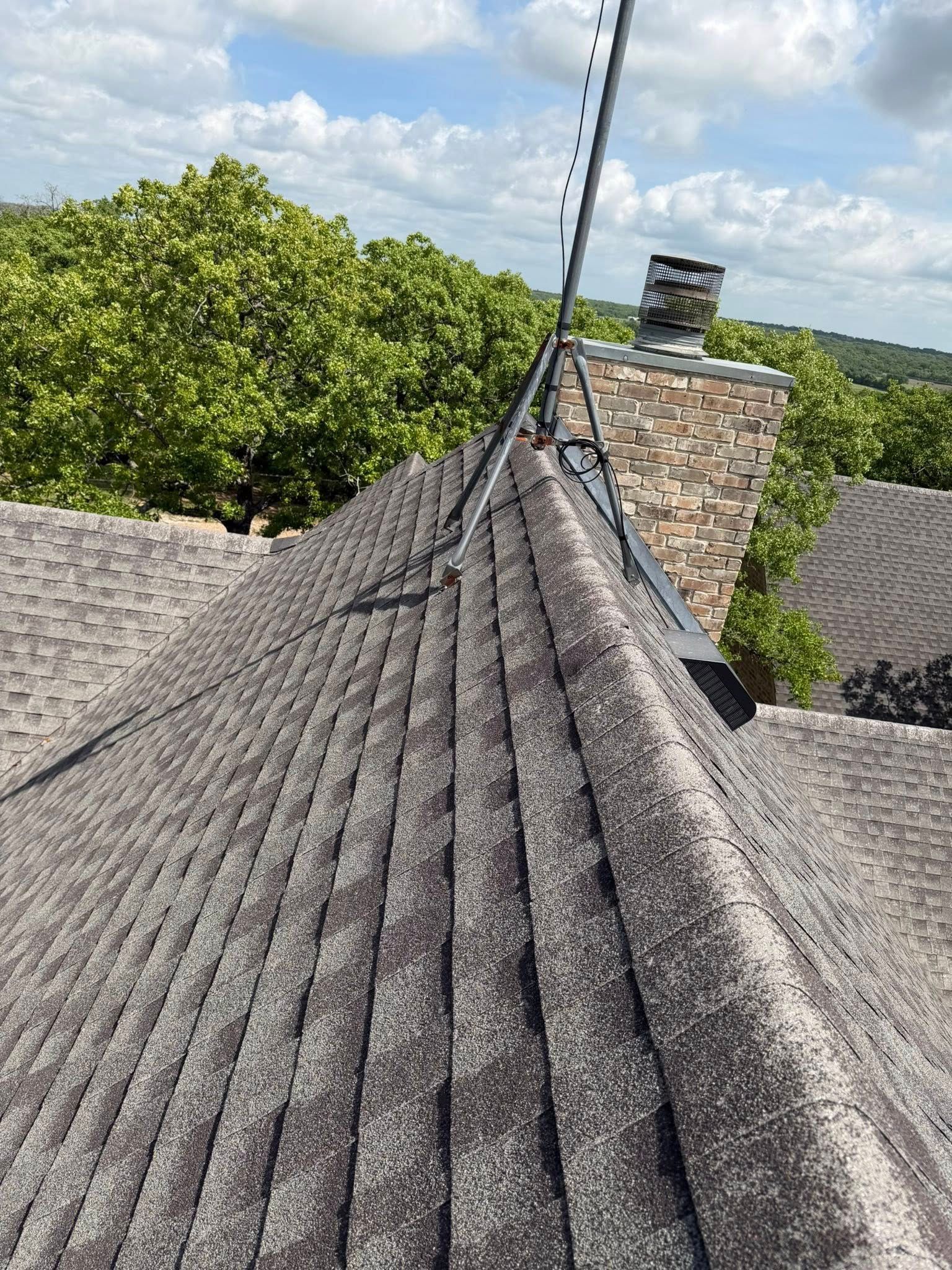 Gray shingled roof with a brick chimney and TV antenna under a blue sky